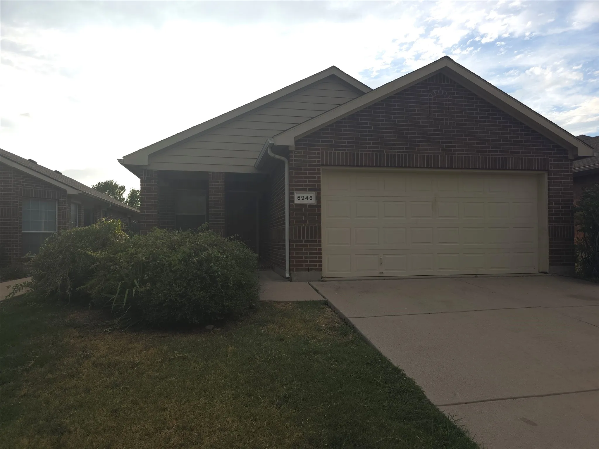 Brick facade with siding accents, attached garage, concrete driveway, and front lawn with shrubbery