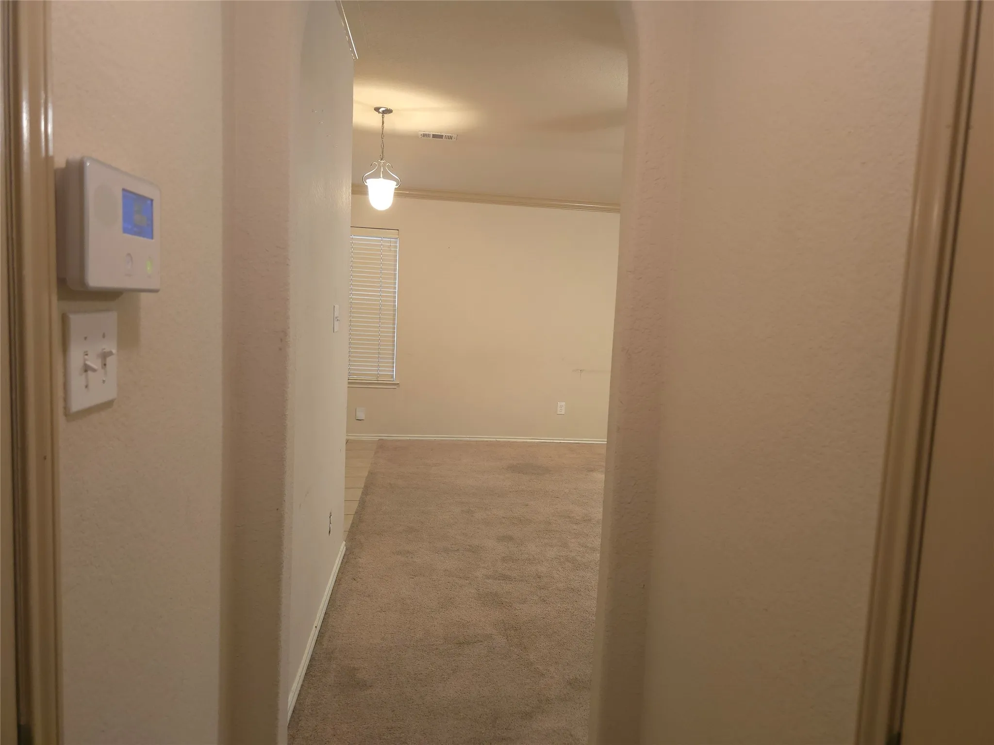 Archway entrance to a room with carpet flooring, a window with horizontal blinds, and a ceiling-mounted pendant light fixture