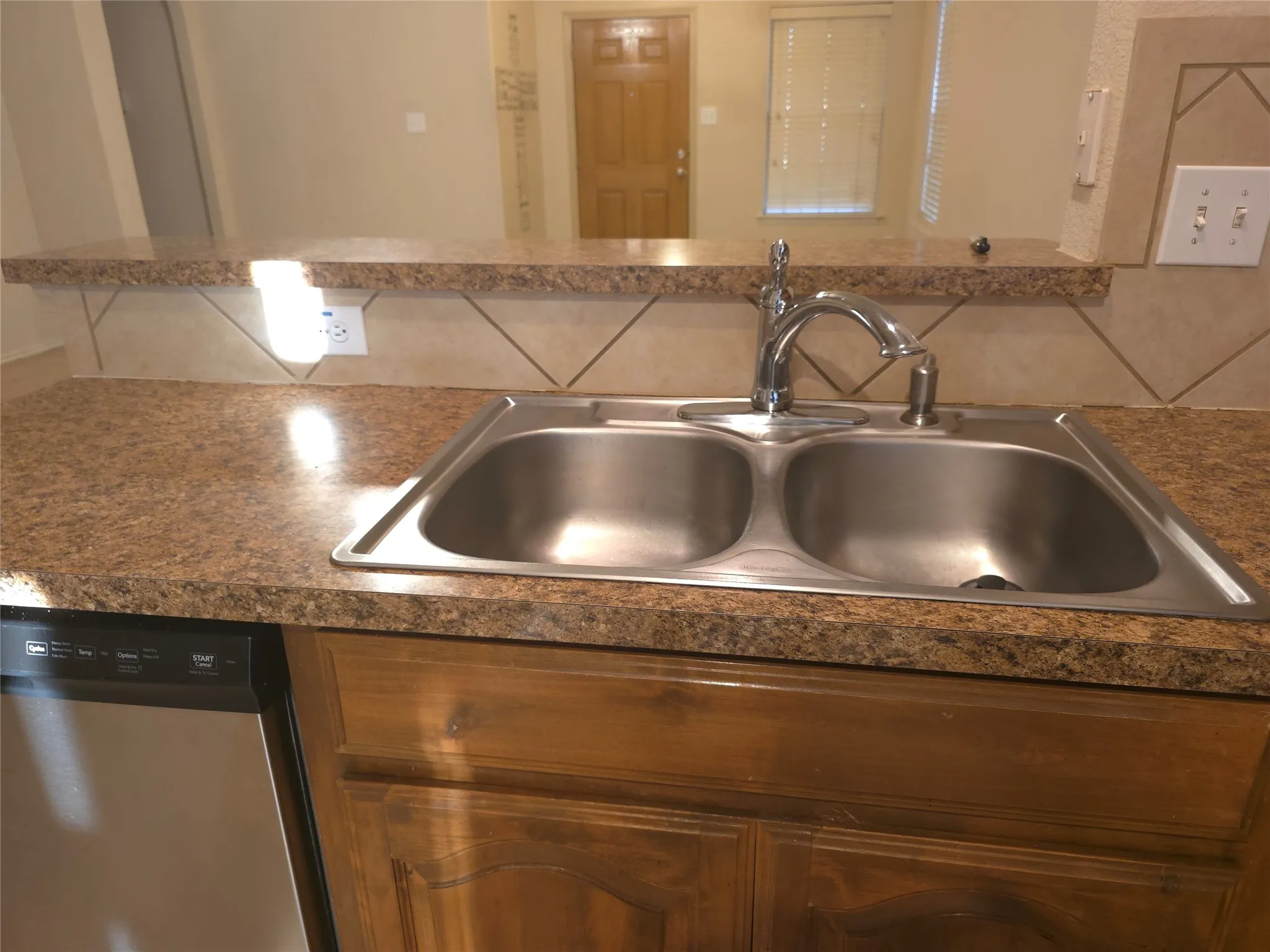 Dual stainless steel sink with chrome faucet, granite-finish countertops, tile backsplash, and wood-finish cabinetry