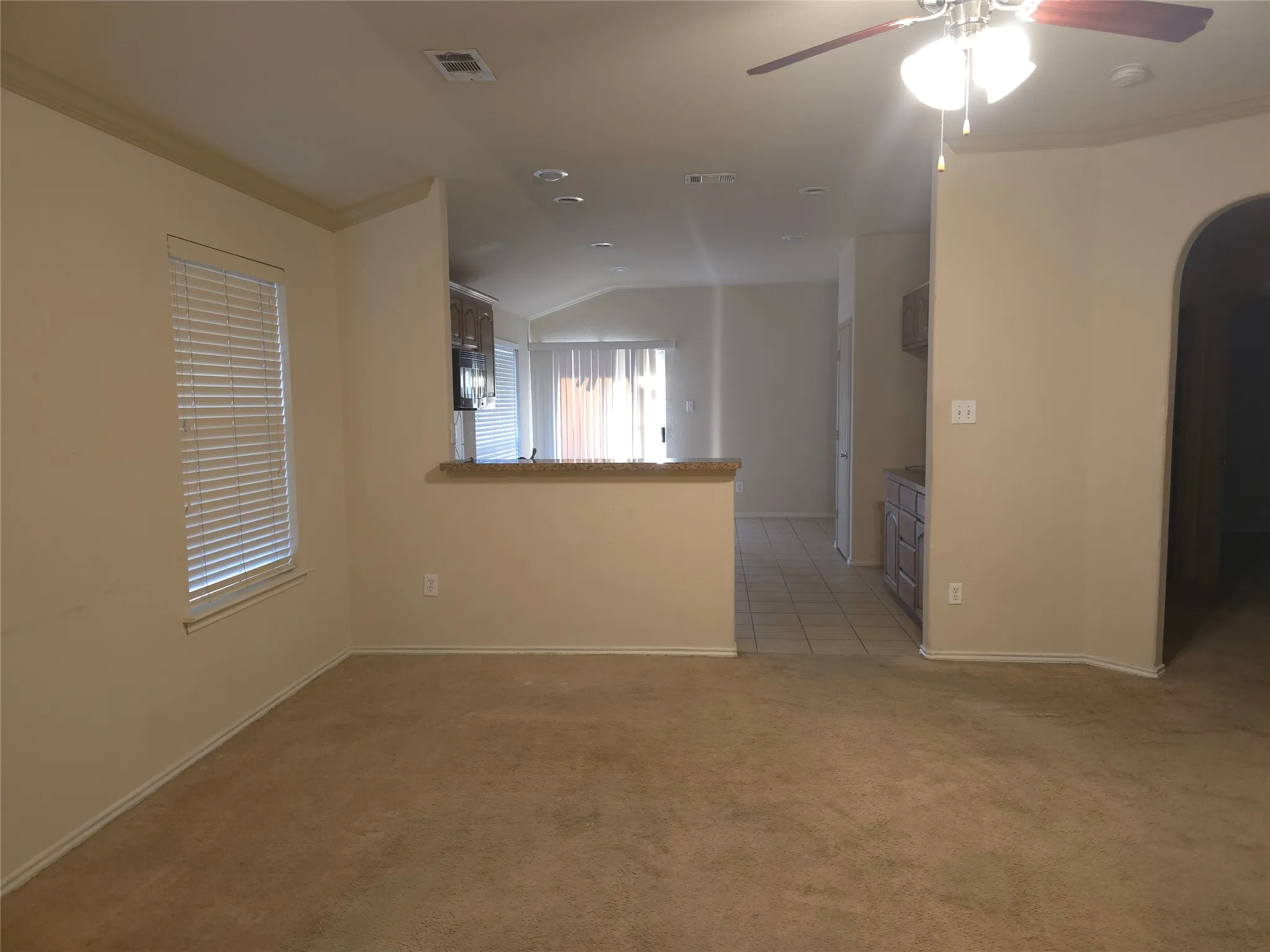 Open-concept living area with carpet flooring, a ceiling fan, and crown molding