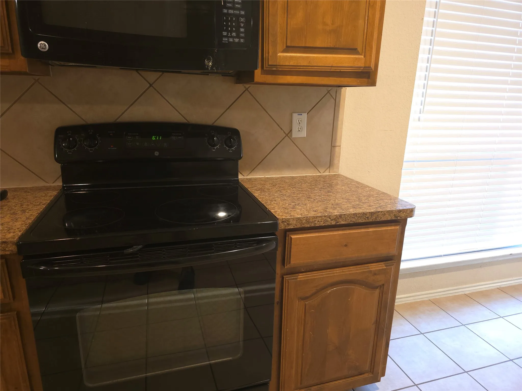 Black range with matching overhead microwave, wood-finish cabinetry, and patterned tile backsplash