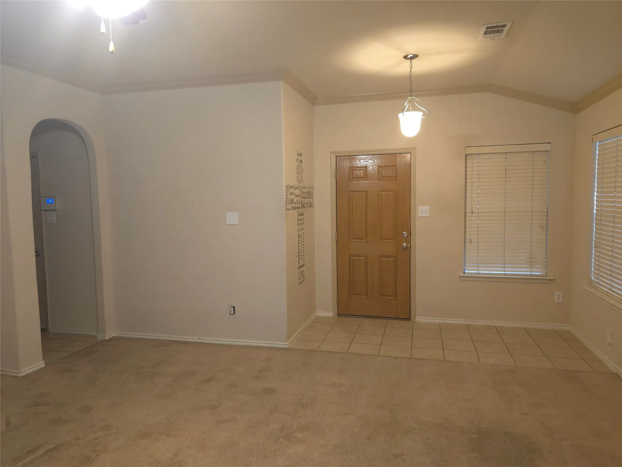 Entry area with tile flooring and a light wood-finish door, featuring a suspended pendant light fixture and an arched doorway