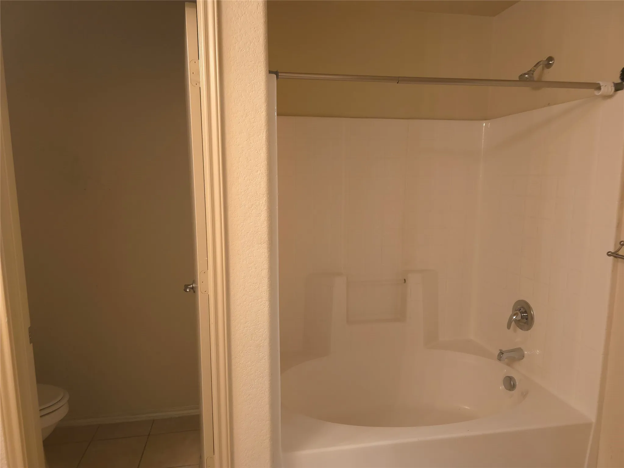 Built-in white bathtub with integrated shower, chrome fixtures, and a separate water closet with tiled flooring