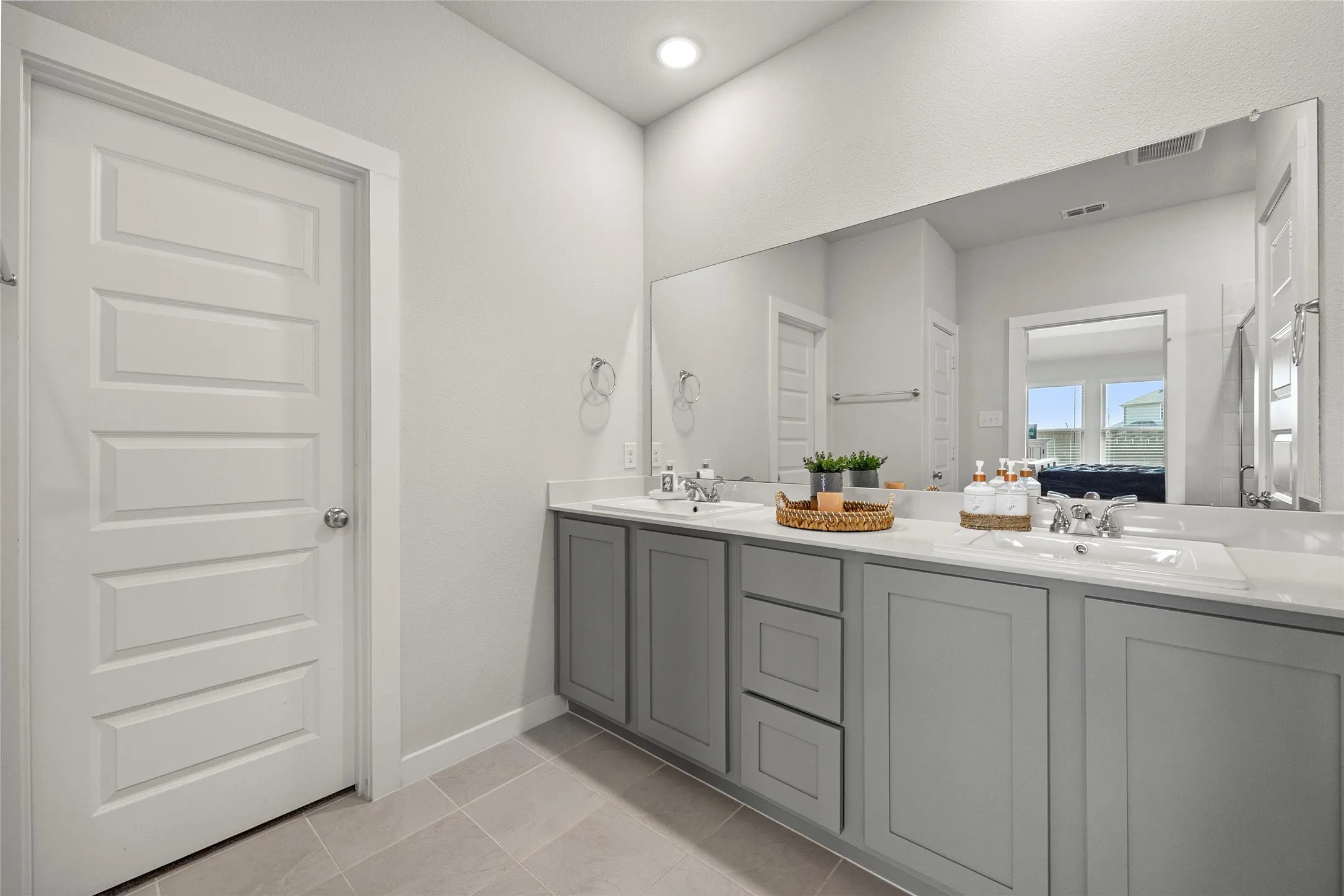 Dual vanity with gray shaker cabinetry, integrated sinks, chrome fixtures, and a full-width mirror