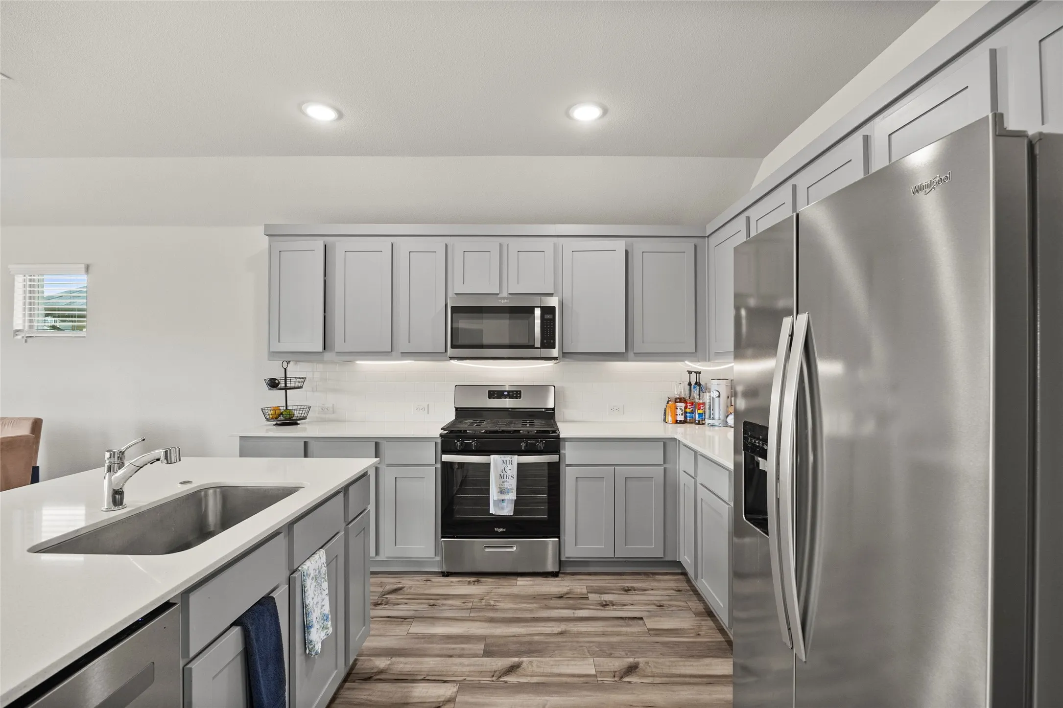 Modern kitchen featuring light gray cabinetry, stainless steel appliances, white countertops, a large island with an undermount sink, and wood-finish flooring