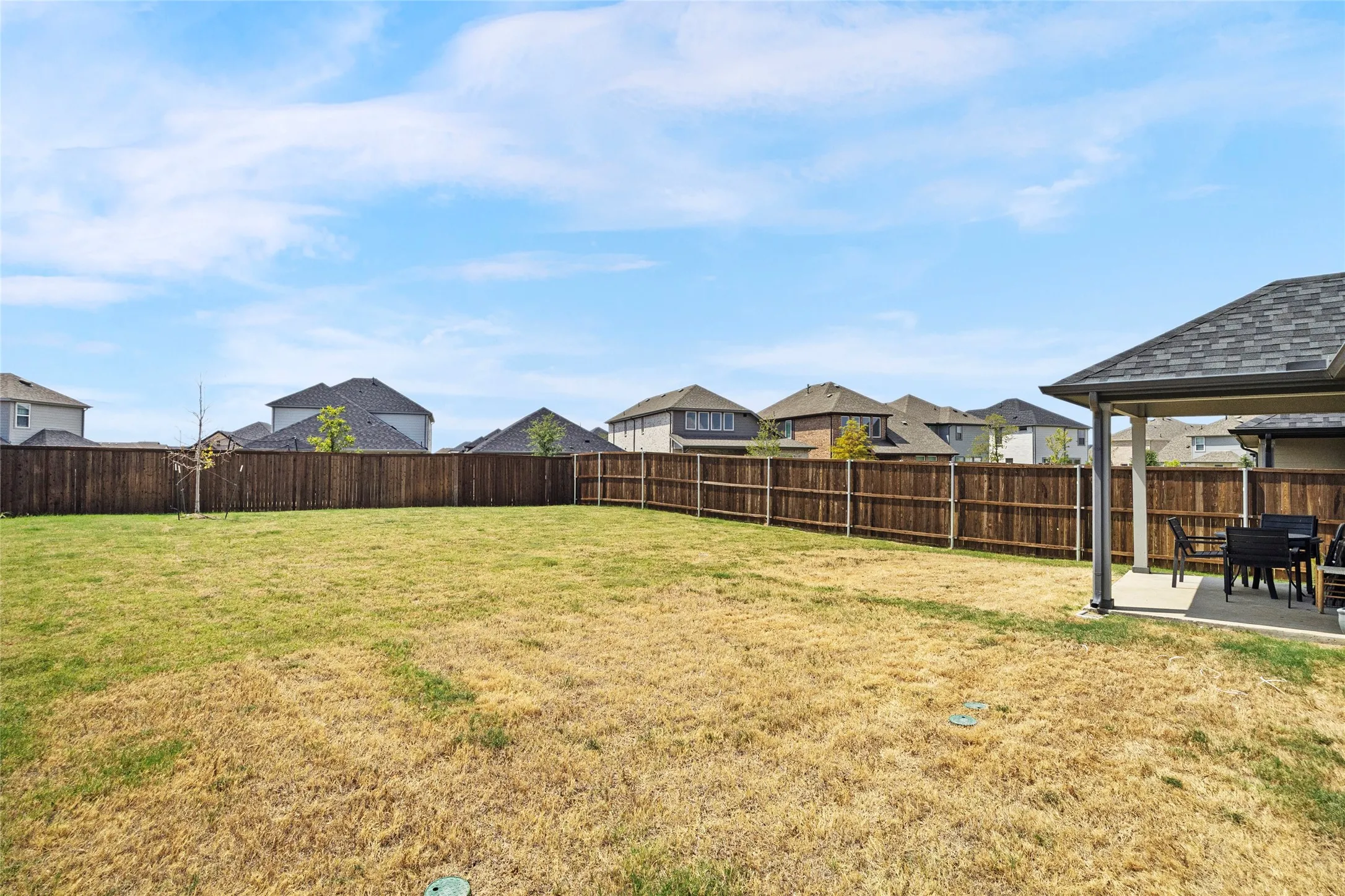 Expansive backyard featuring a privacy fence, covered patio with concrete flooring, and an asphalt shingle roof