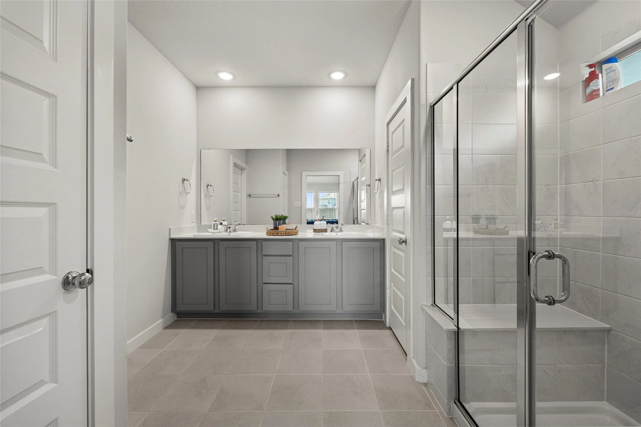 Dual vanity with undermount sinks, stone-finish countertop, large mirror, glass-enclosed shower, and recessed lighting