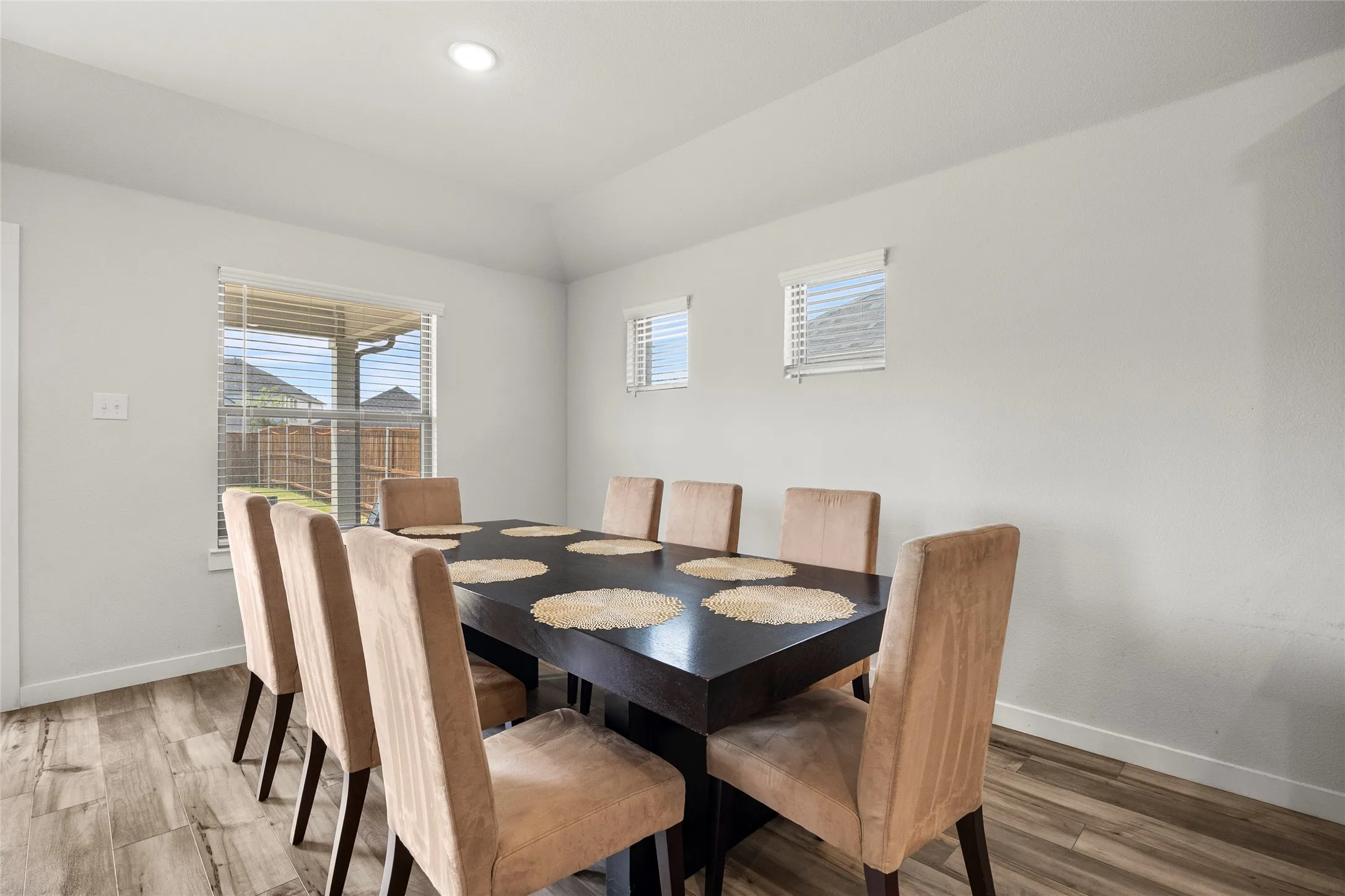 Vaulted ceiling with recessed lighting, wood-finish flooring, and multiple windows with blinds
