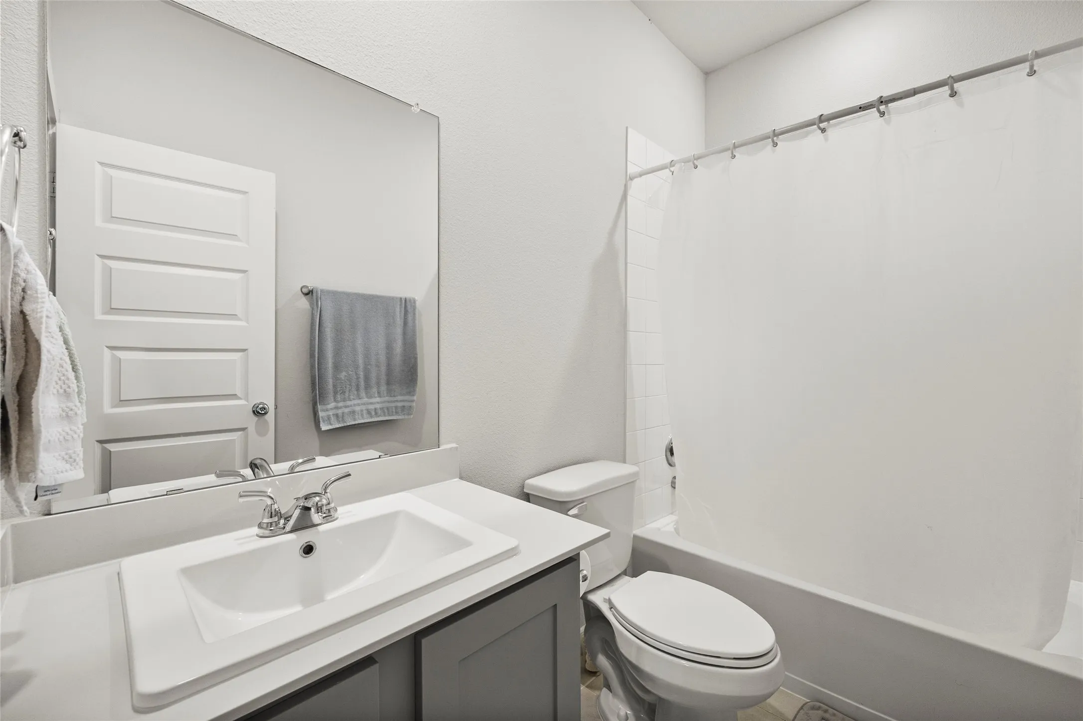 Bathroom featuring a single vanity, integrated sink, gray cabinetry, and a full-size bathtub with shower