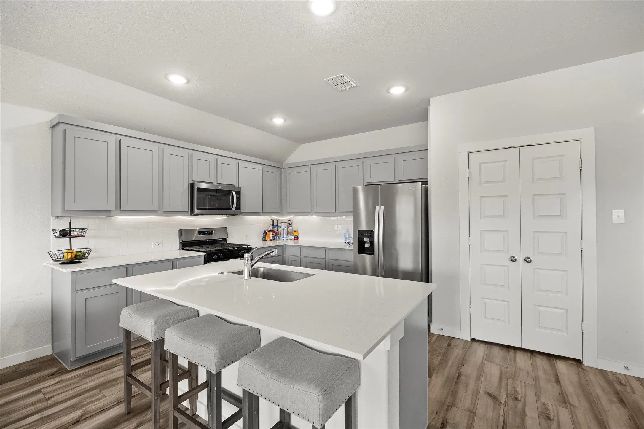 Kitchen featuring gray cabinetry, stainless steel appliances, a center island with sink, white countertops, and wood-finish flooring