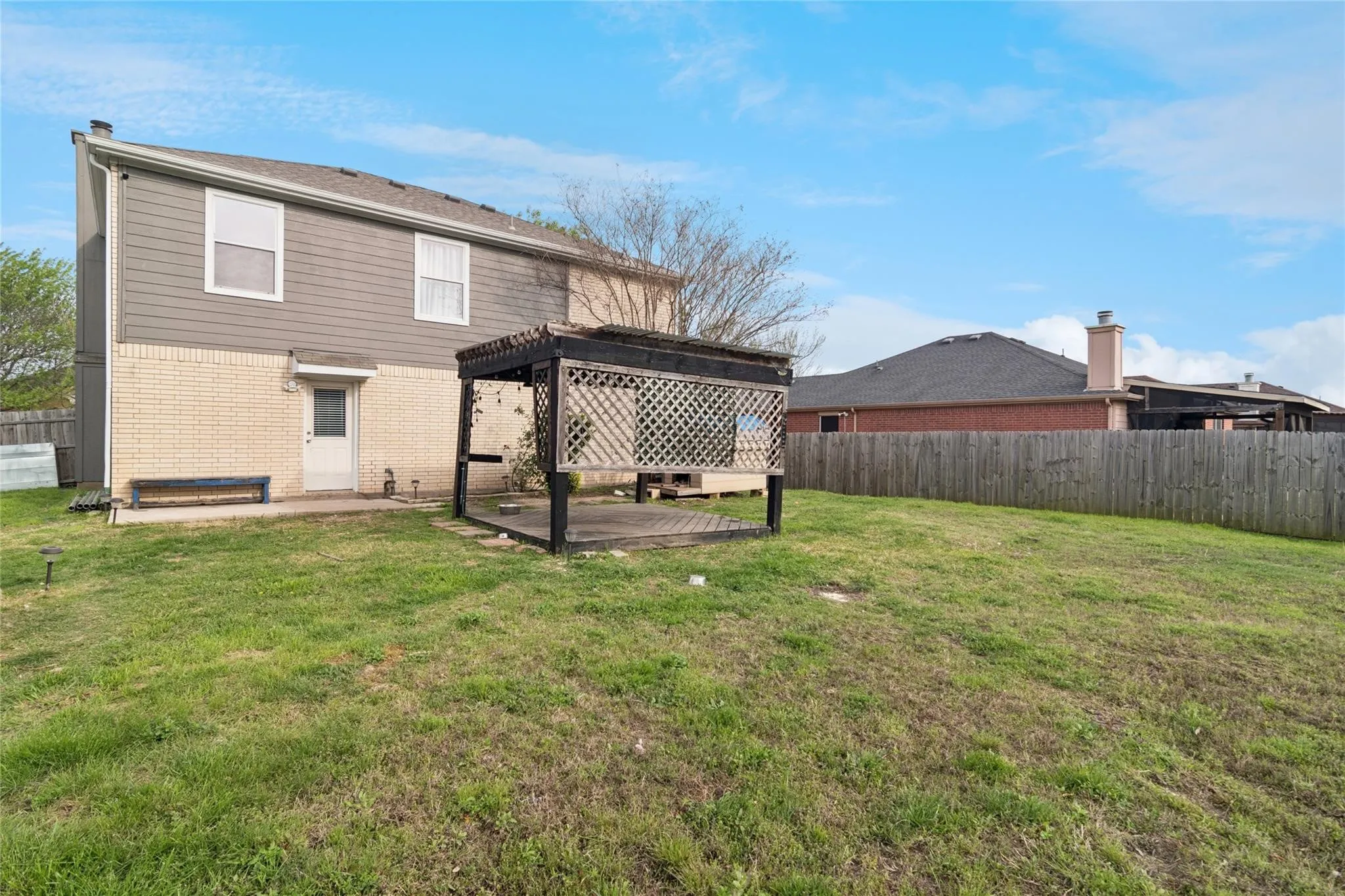 Expansive rear yard featuring a wooden pergola with a latticed roof, a concrete patio, and a privacy fence