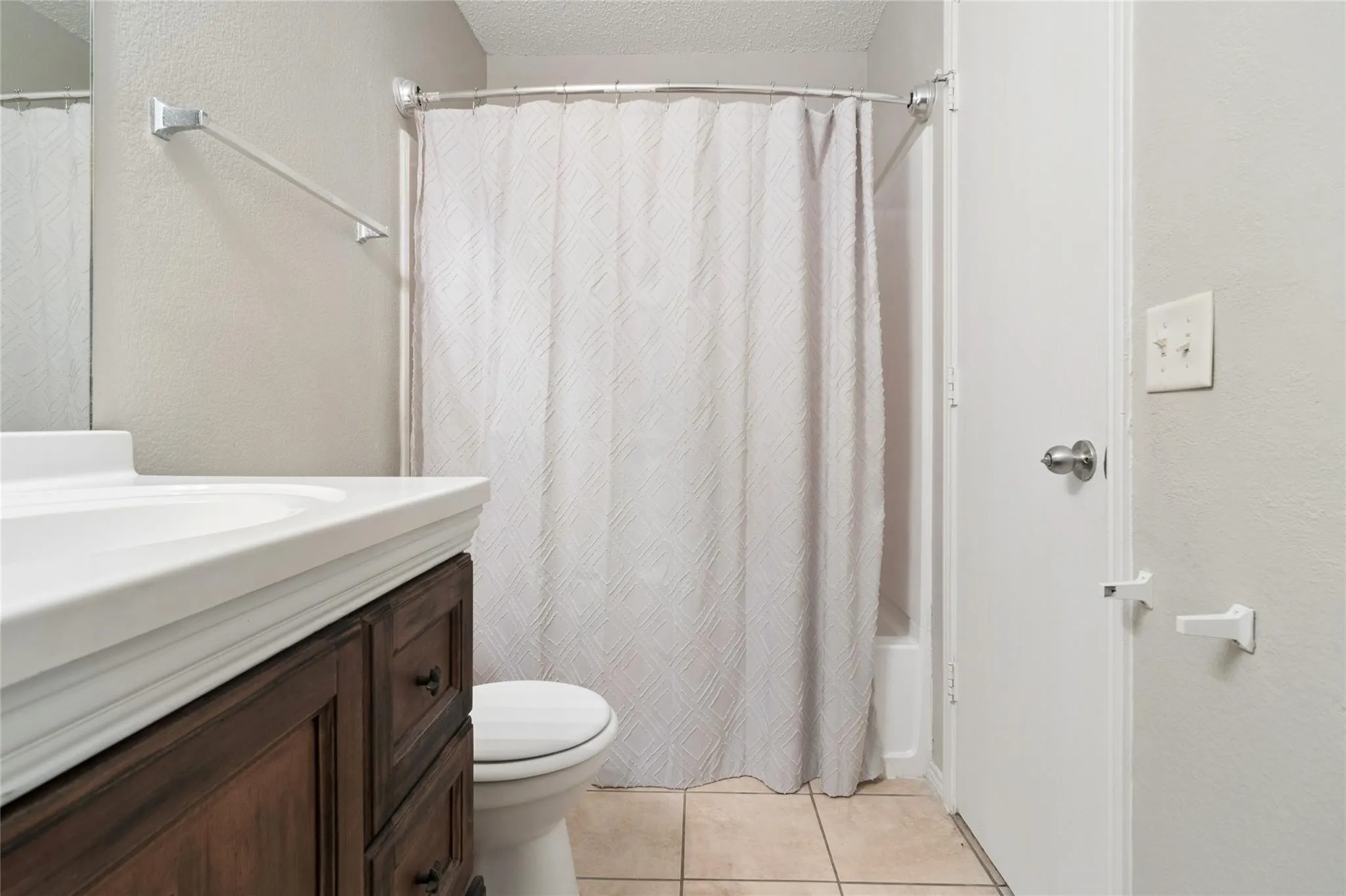 White vanity with integrated sink, dark wood-finish cabinet, tub with shower, and tile flooring