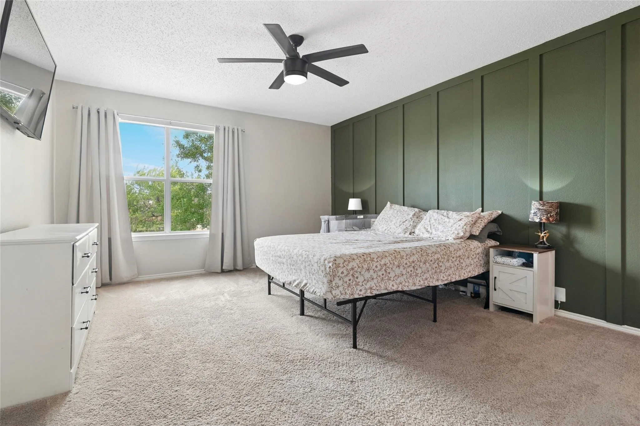 Textured accent wall, ceiling fan with light, large window, and light-toned carpeting