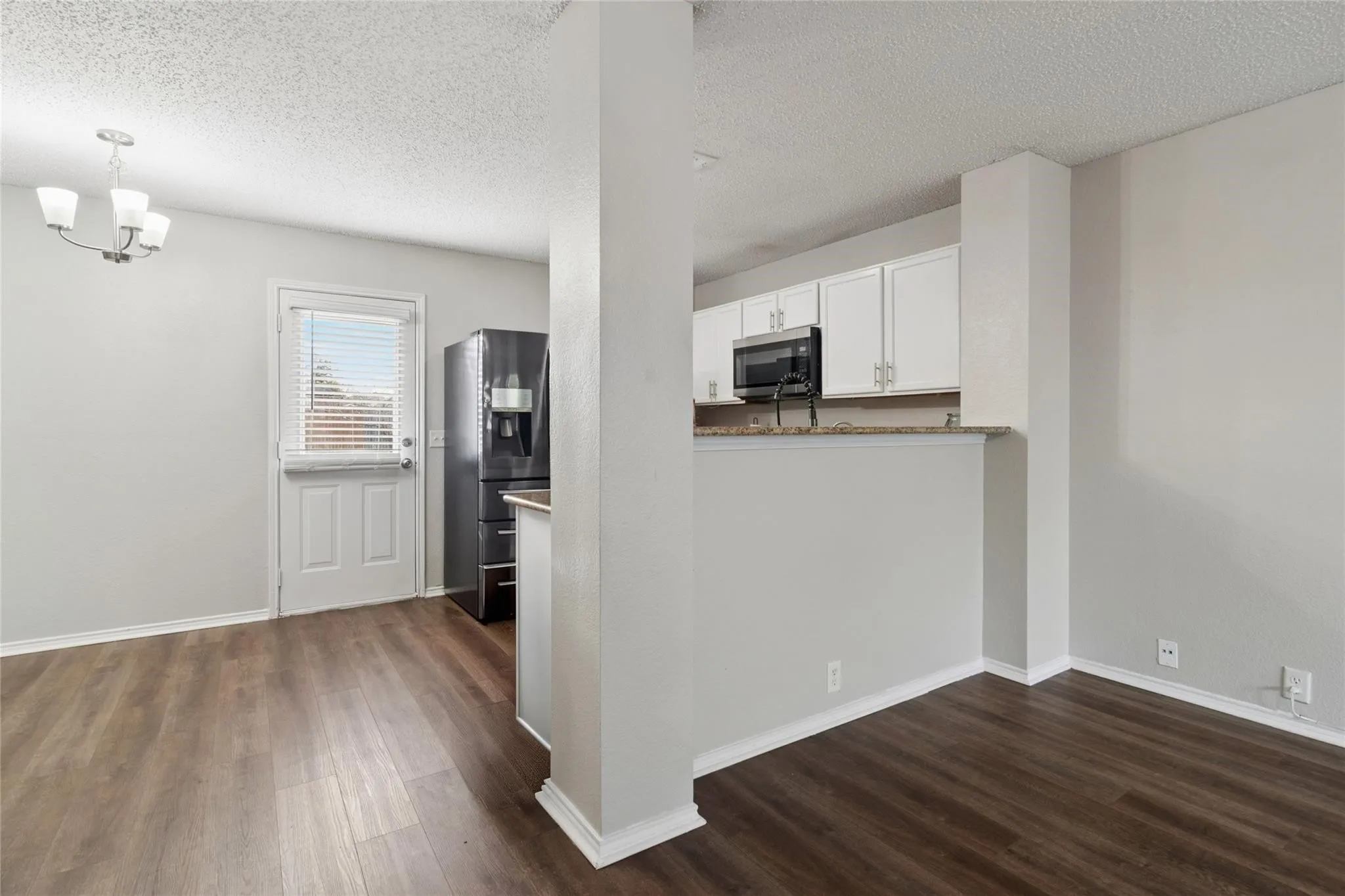 Wood-finish flooring, white cabinetry, dark refrigerator, built-in microwave, and a breakfast bar with a stone countertop