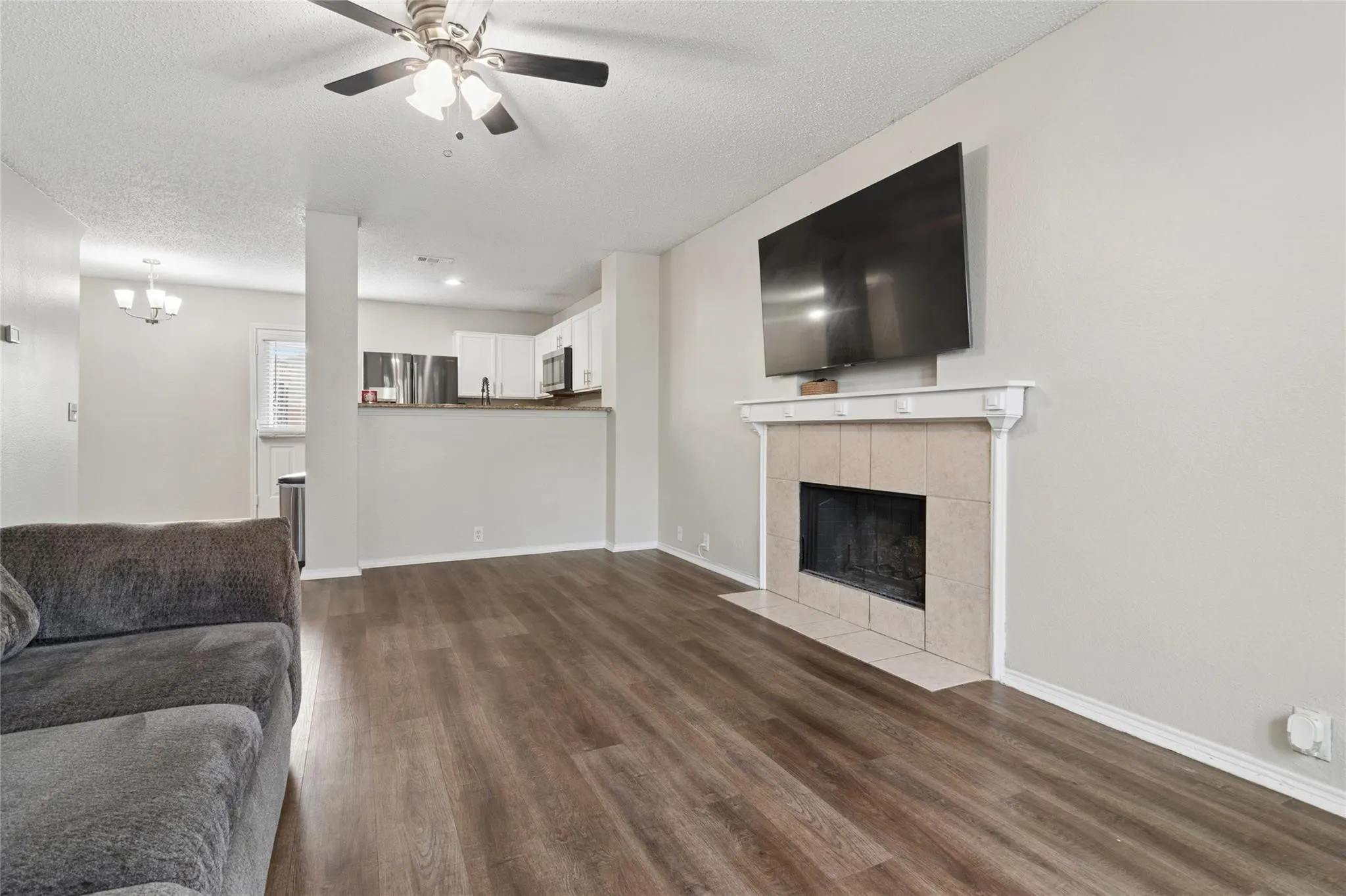 Spacious room featuring wood-finish flooring, a ceiling fan with integrated lighting, and a fireplace with a tile surround and decorative mantel