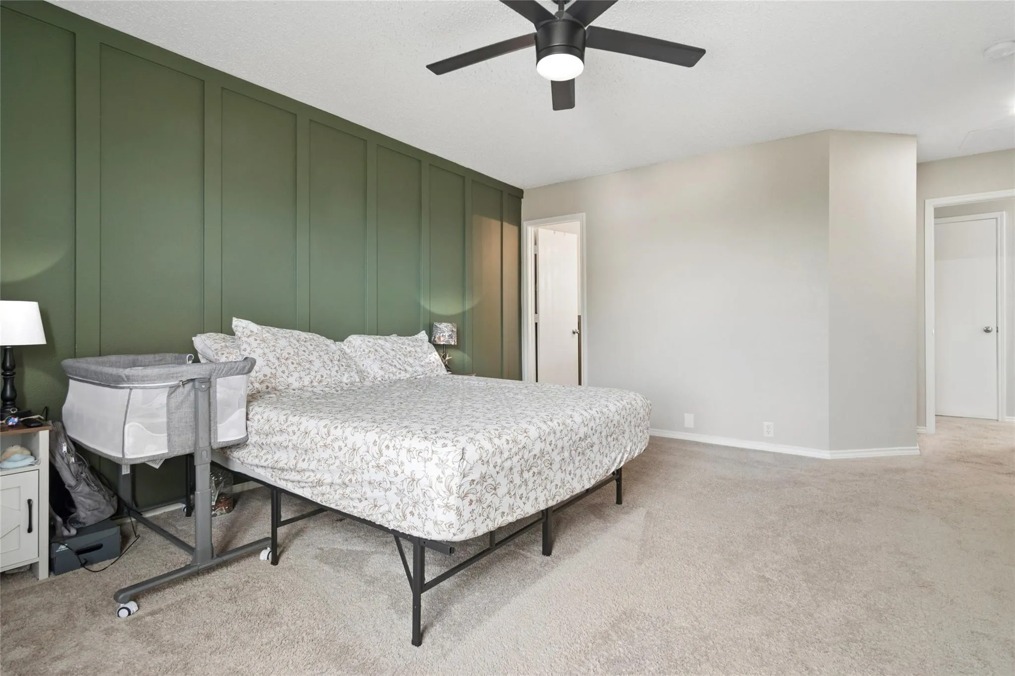 Accent wall with vertical paneling, light gray carpet, ceiling fan with integrated lighting, multiple doorways, and neutral wall paint