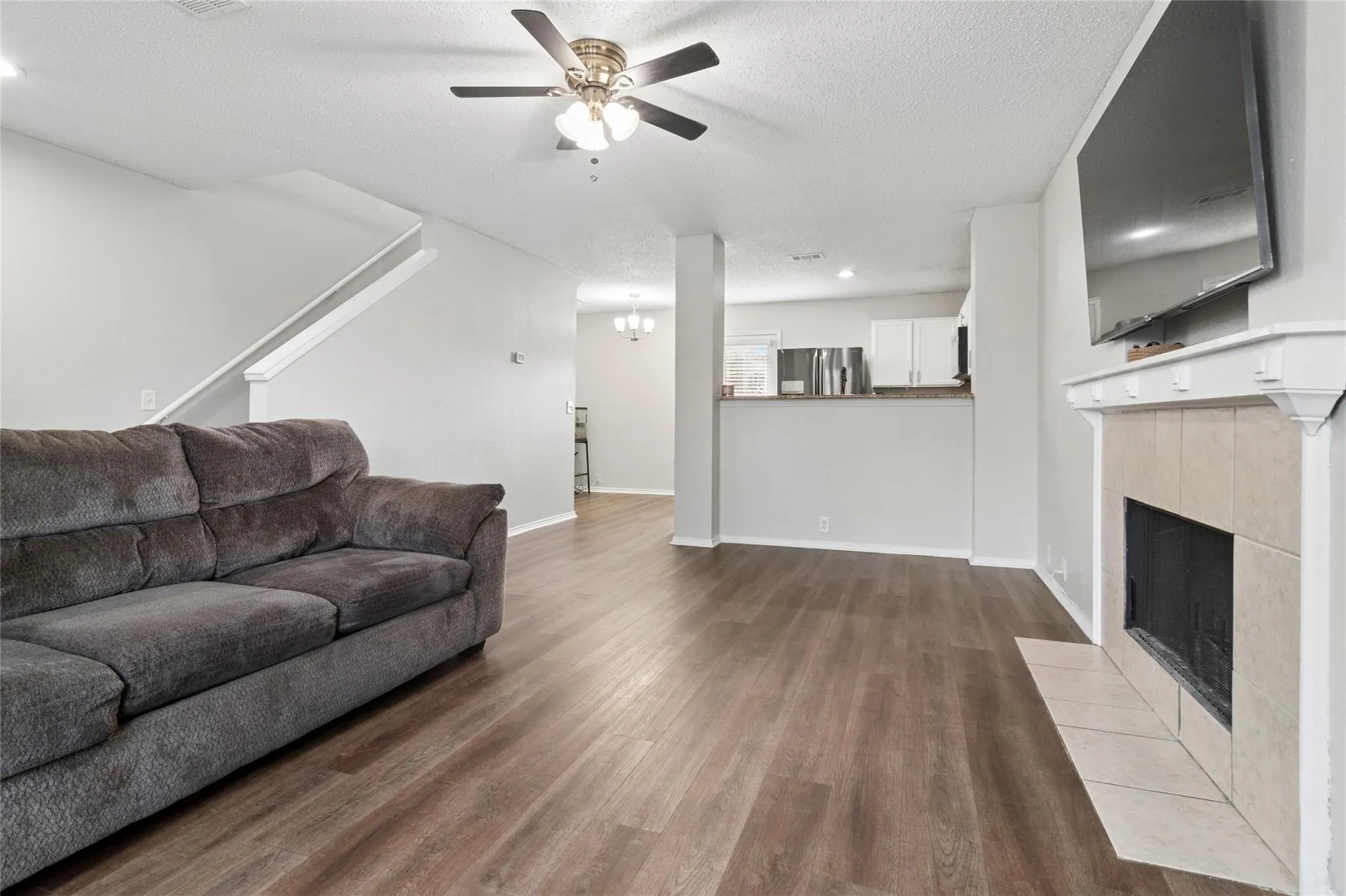Expansive living area featuring wood-finish flooring, a ceiling fan, and a tiled fireplace with a mantel