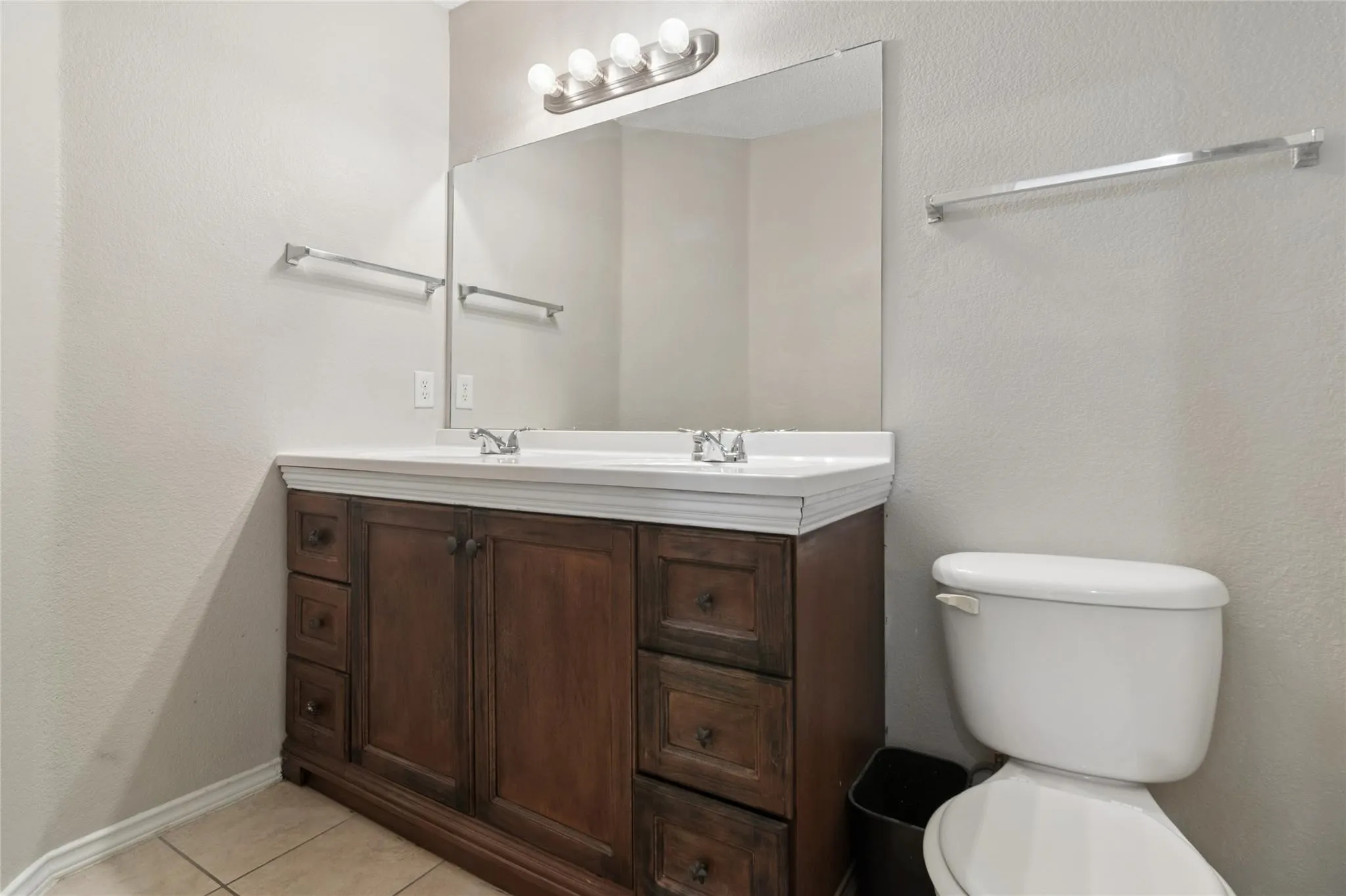 Dual-sink vanity with wood-finish cabinetry, white countertop, and prominent mirror