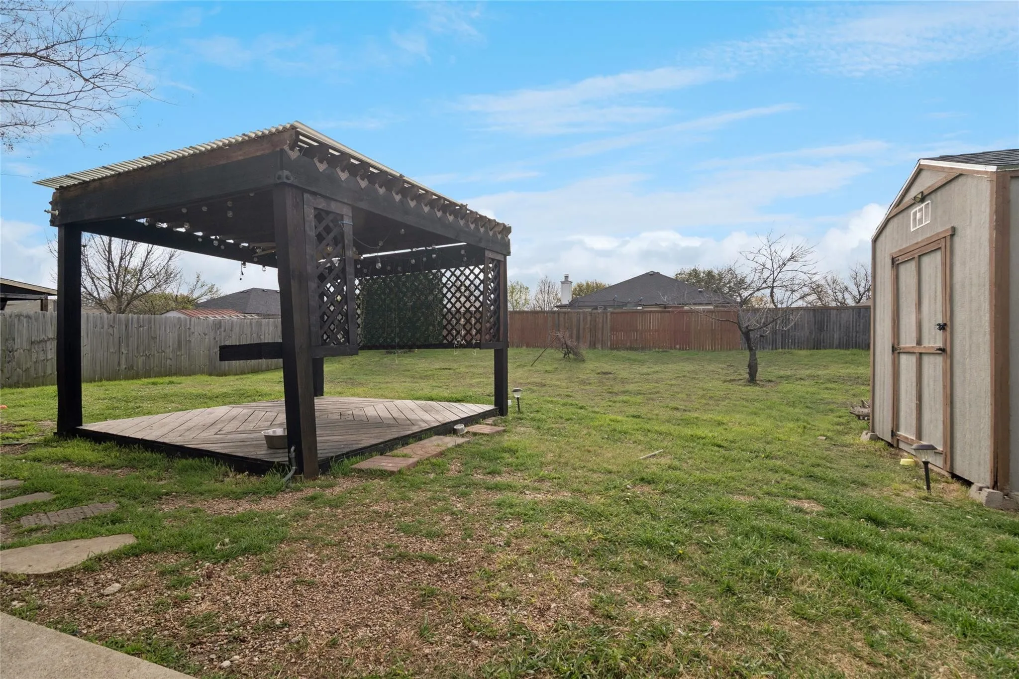 Expansive backyard featuring a wood-finish pergola with a translucent roof, a dedicated storage shed, a wood-finish deck, and a privacy fence