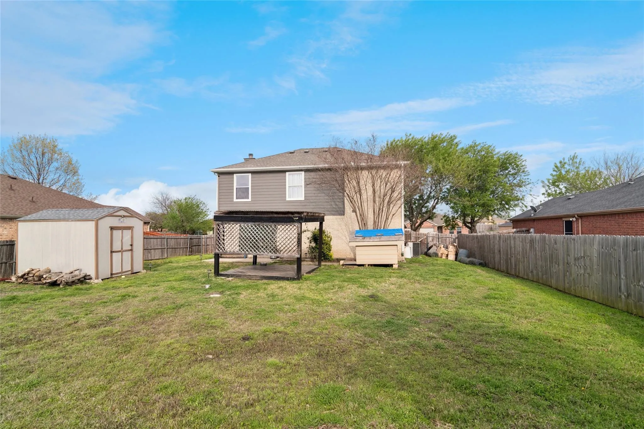 Expansive backyard featuring a partial privacy fence, a detached storage shed, a wood pergola, and a multi-level exterior