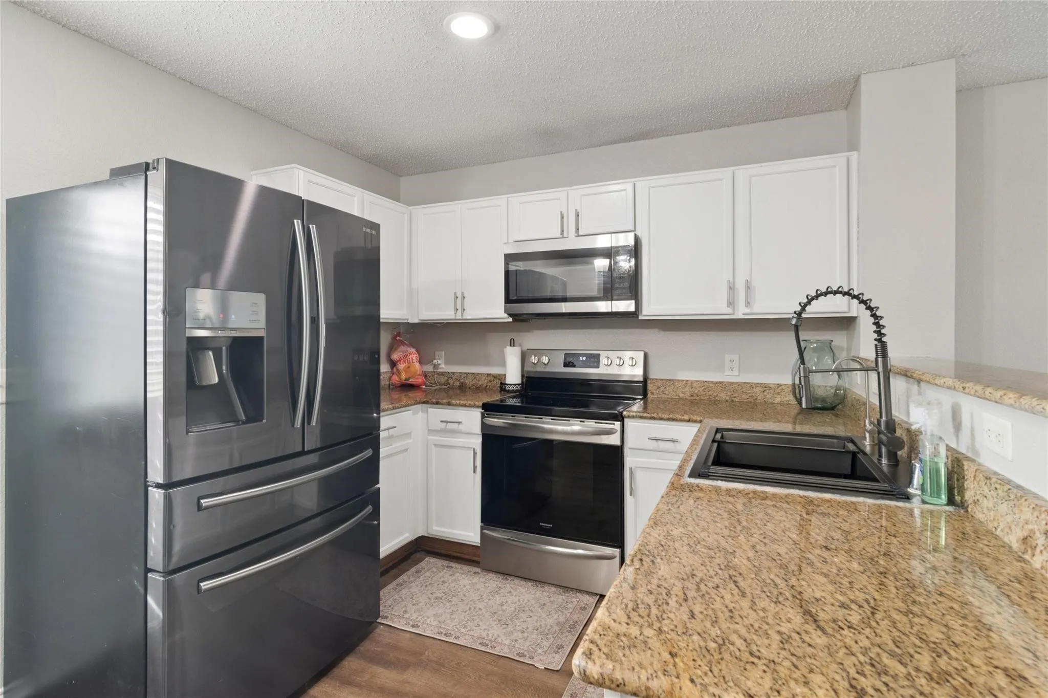 Kitchen featuring white cabinetry, stainless steel appliances, speckled stone countertops, and a black sink with a flexible hose faucet