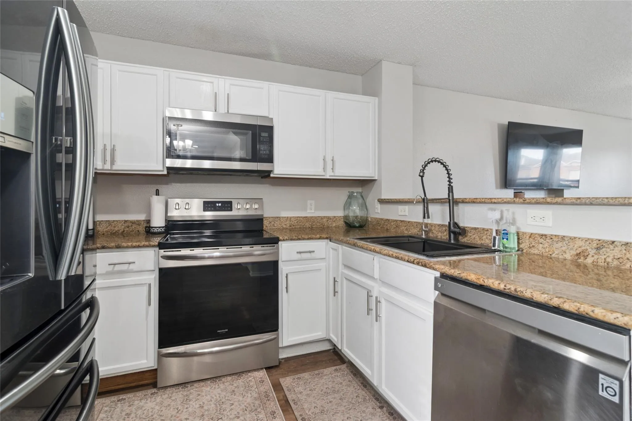 White cabinetry with stainless steel hardware, granite-style countertops, stainless steel appliances, a black sink, and a gooseneck faucet