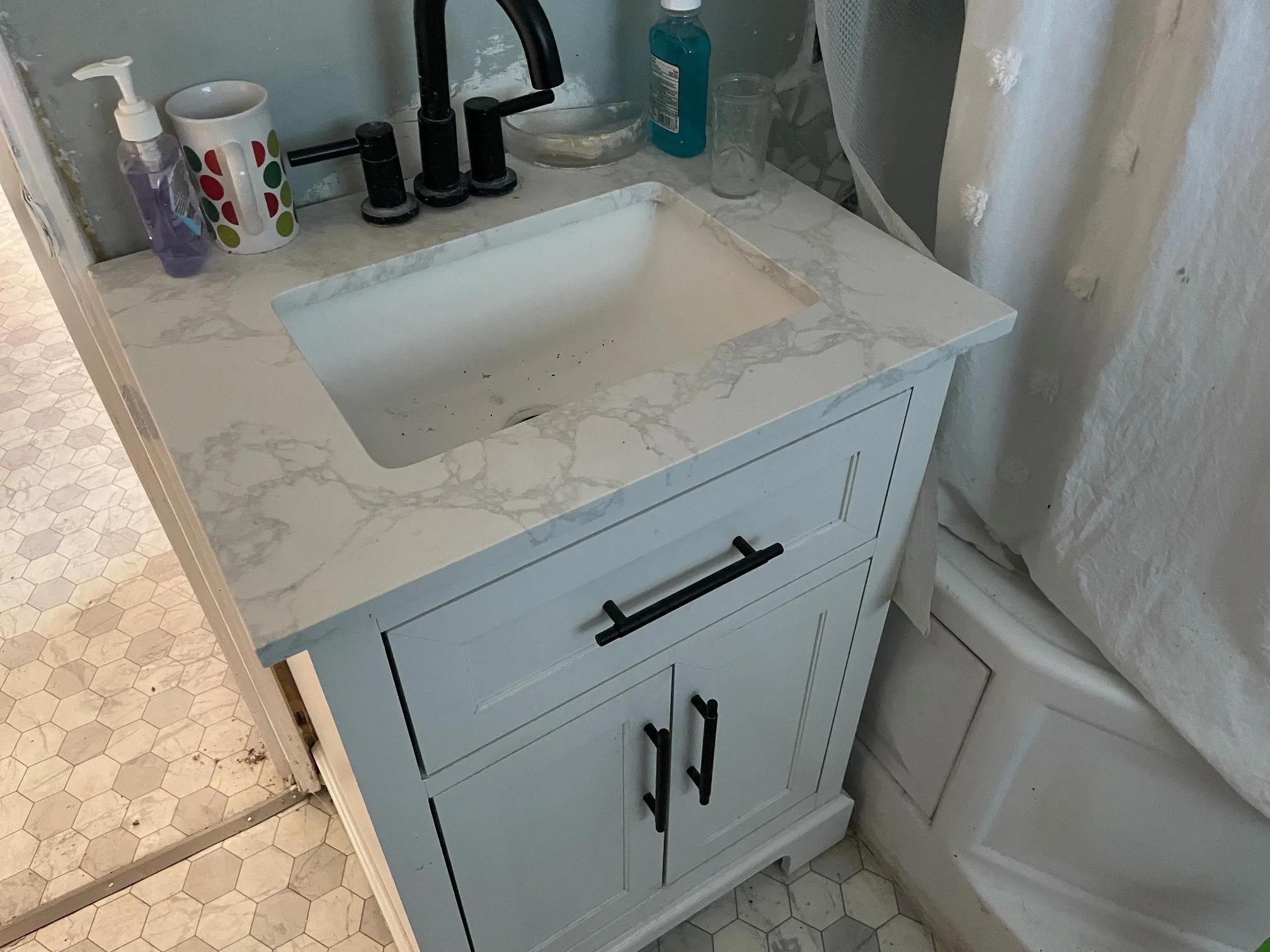 White shaker vanity with black hardware, integrated sink with a stone-finish countertop, and a black faucet