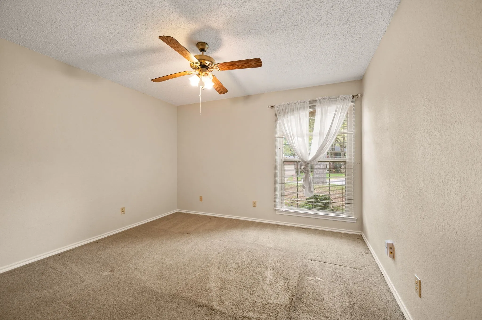 Neutral-toned room featuring wall-to-wall carpeting, a multi-blade ceiling fan with an integrated light fixture, and a large window