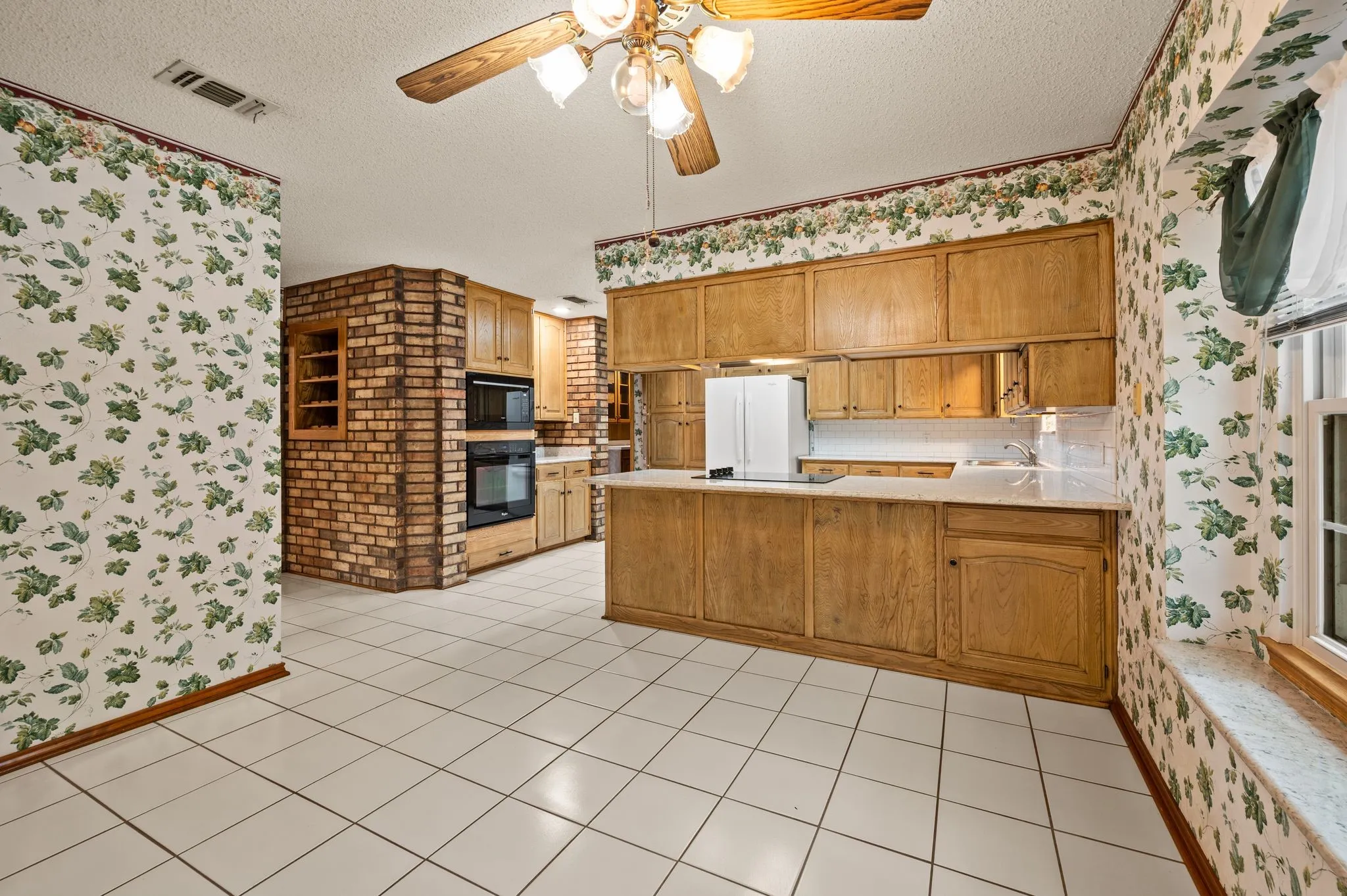 Kitchen featuring a large brick column, custom cabinetry, a peninsula countertop, built-in double wall ovens, and ceramic tile flooring