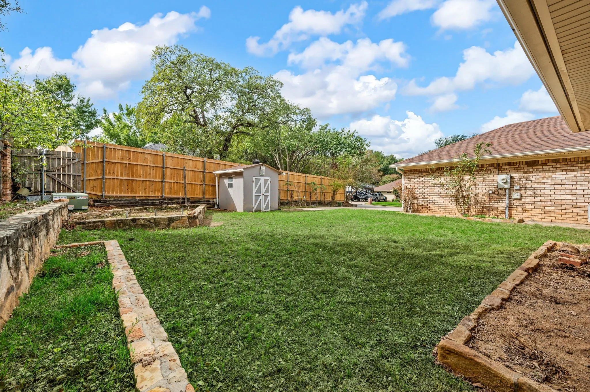 Backyard featuring a brick exterior, stone retaining walls, wood-privacy fencing, and a detached storage shed