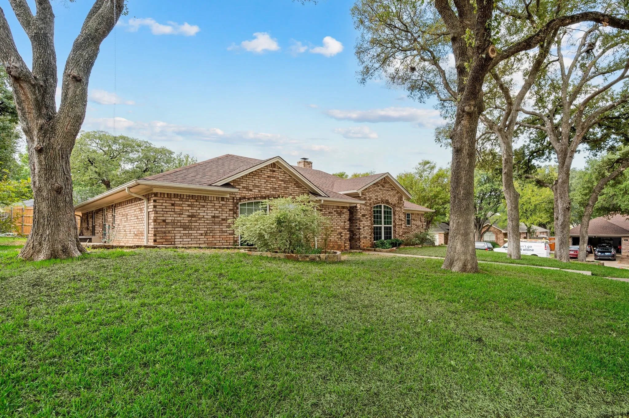 Single-story brick exterior featuring a hipped roof, arched windows, and mature trees on a landscaped lot