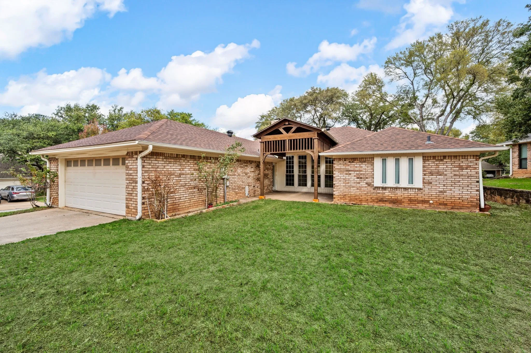Single-story brick exterior featuring a multi-gabled roofline, an attached two-car garage, and a covered front entry with wooden lattice detailing