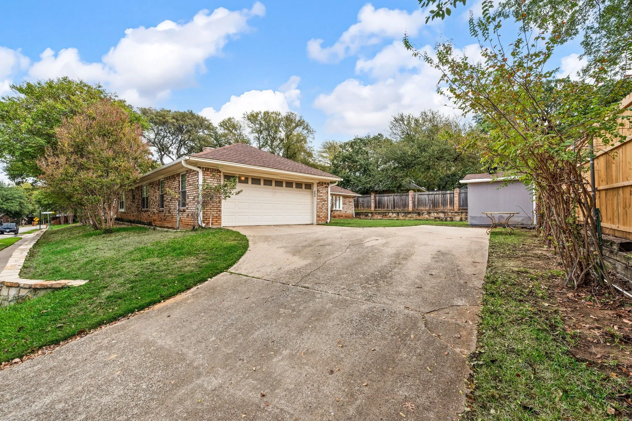 Brick exterior featuring a multi-car garage, concrete driveway, and wood-panel fencing