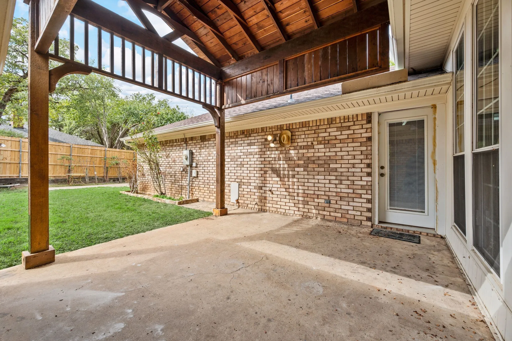 Covered patio featuring a timber-frame pergola, concrete flooring, brick exterior wall, and direct access to a fenced backyard
