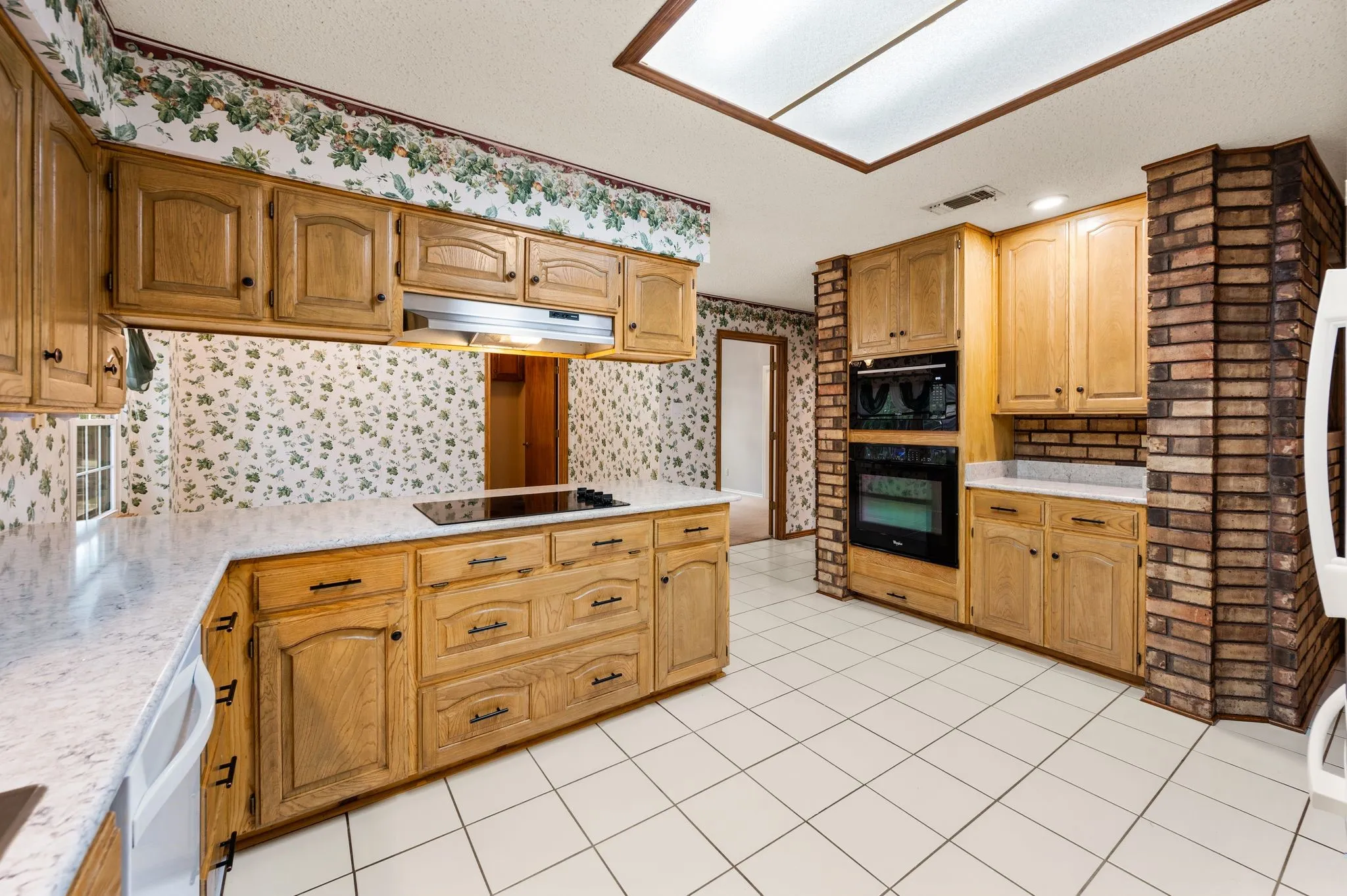 Kitchen featuring light-tone cabinetry, solid surface countertops, a built-in double oven, a smooth cooktop, and a brick pillar surround