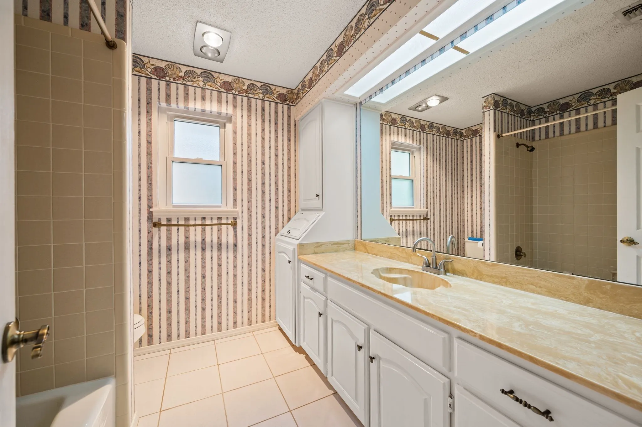 Bathroom featuring a vanity with stone-finish countertop, white cabinetry with built-in hamper, tile flooring, and full-width mirror