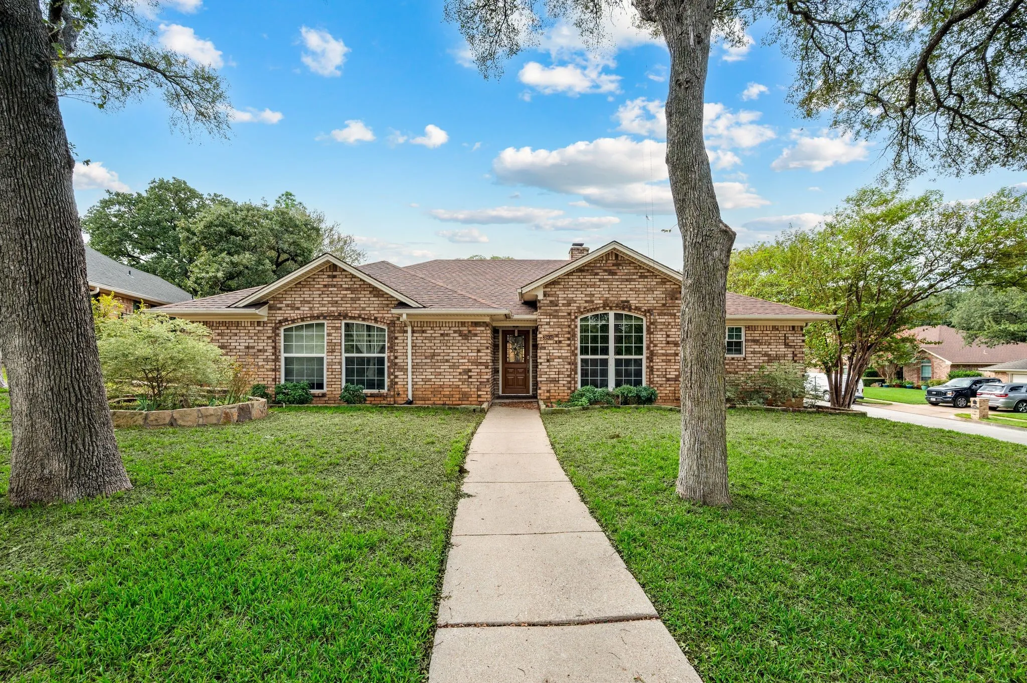 Single-story brick exterior featuring an arched entryway, stone-bordered landscaping, and a concrete walkway