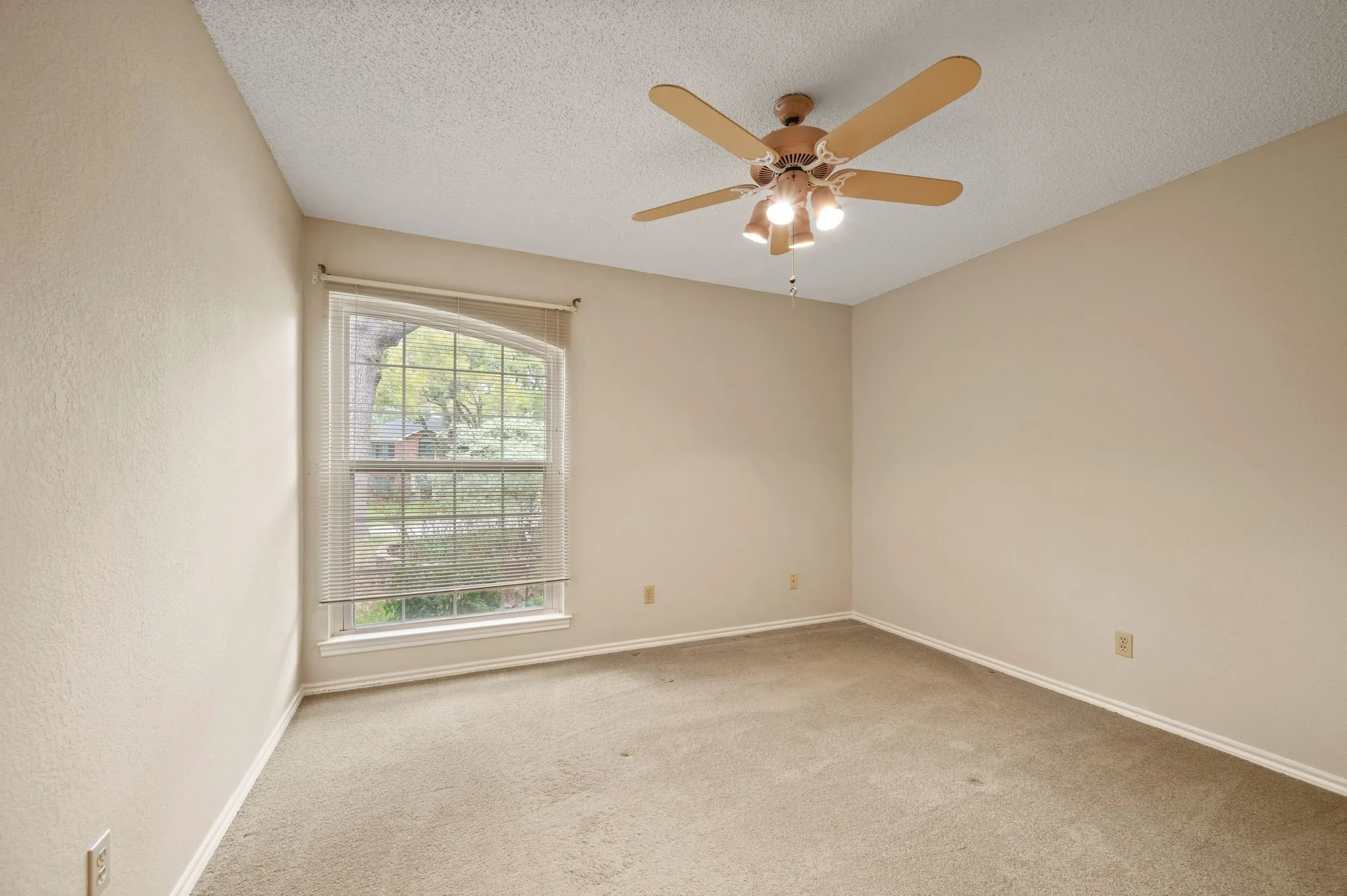 Interior room featuring neutral wall paint, carpeting, a ceiling fan with integrated lighting, and a multi-pane window with an arched top