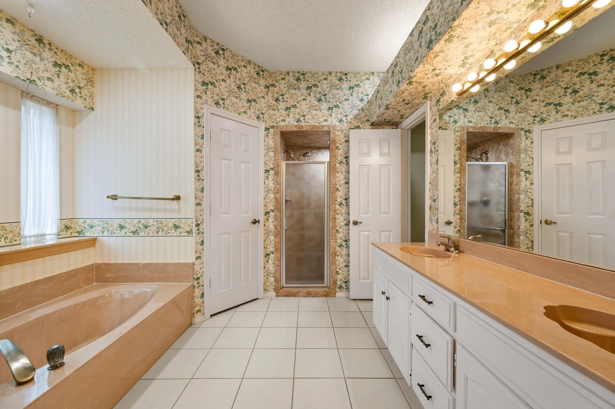 Bathroom featuring a deep-soaking tub with tile surround, white cabinetry, dual-sink vanity with countertop, glass-enclosed shower, and full-width vanity mirror