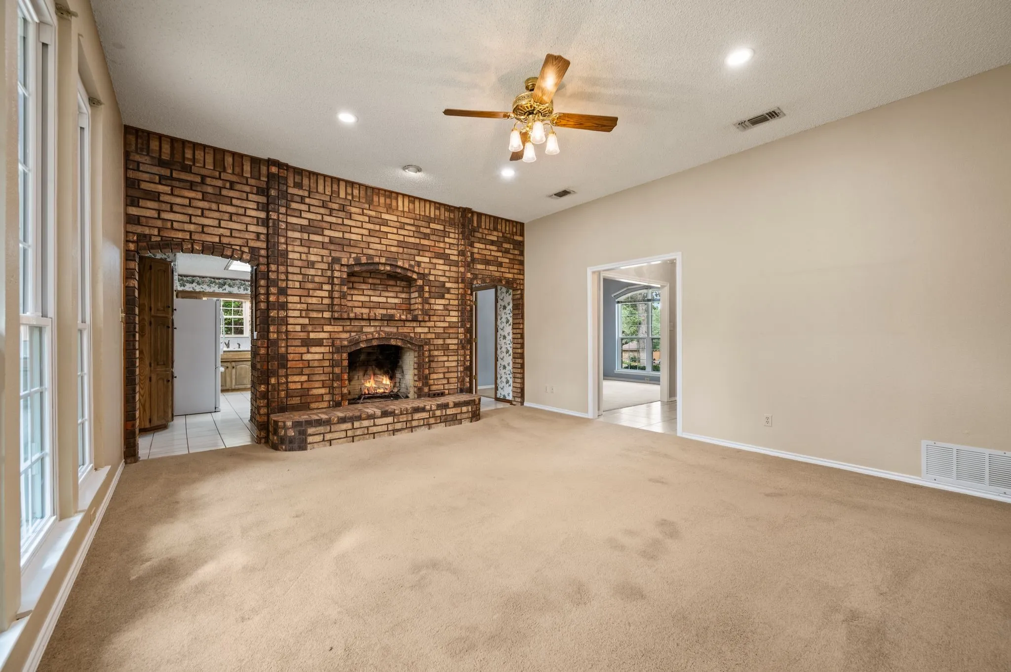 Expansive room featuring a floor-to-ceiling brick fireplace with a built-in recessed niche, high ceilings, recessed lighting, and a multi-light ceiling fan