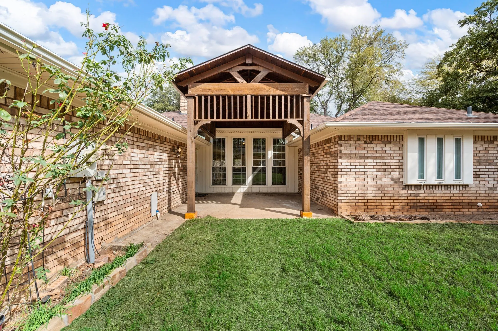 Brick exterior featuring a covered patio with a wooden pergola, multi-pane windows, and a manicured lawn