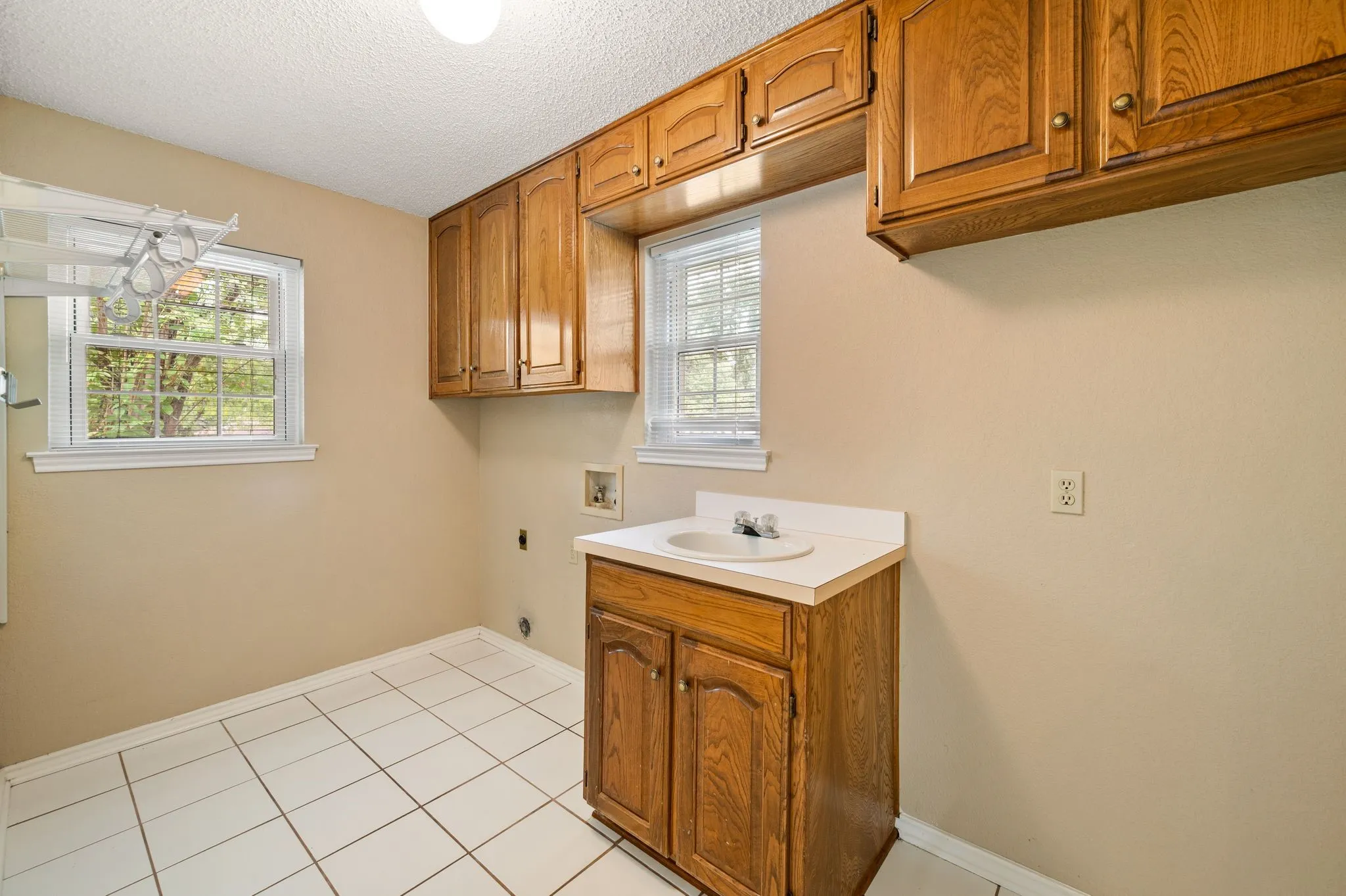 Utility area featuring wood cabinetry, white tile flooring, dual windows, and a built-in vanity with a drop-in sink