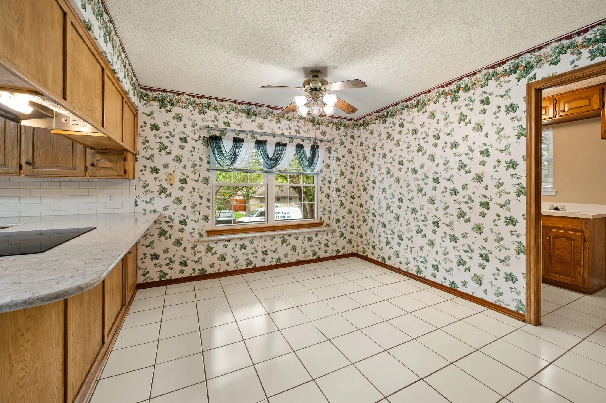 Kitchen featuring light-toned cabinetry, light-colored countertops, white ceramic tile flooring, and a ceiling-mounted light fixture with fan