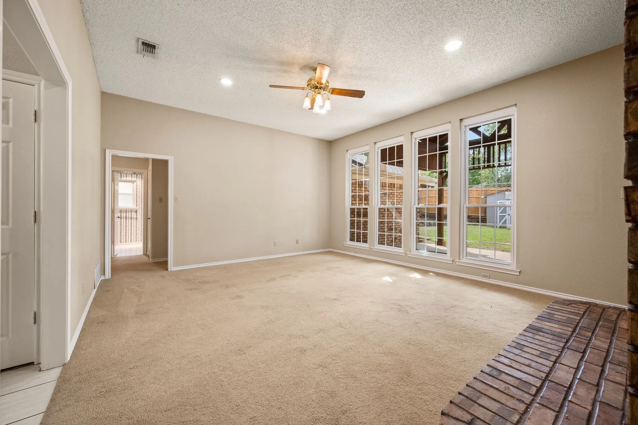 Spacious interior featuring a brick hearth, wall-to-wall carpeting, recessed lighting, a ceiling fan, and large windows with paneled detailing