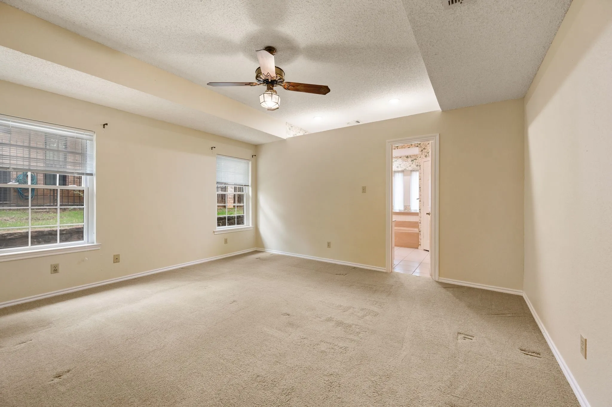 Room featuring a tray ceiling, ceiling fan with light kit, neutral carpeting, and dual windows