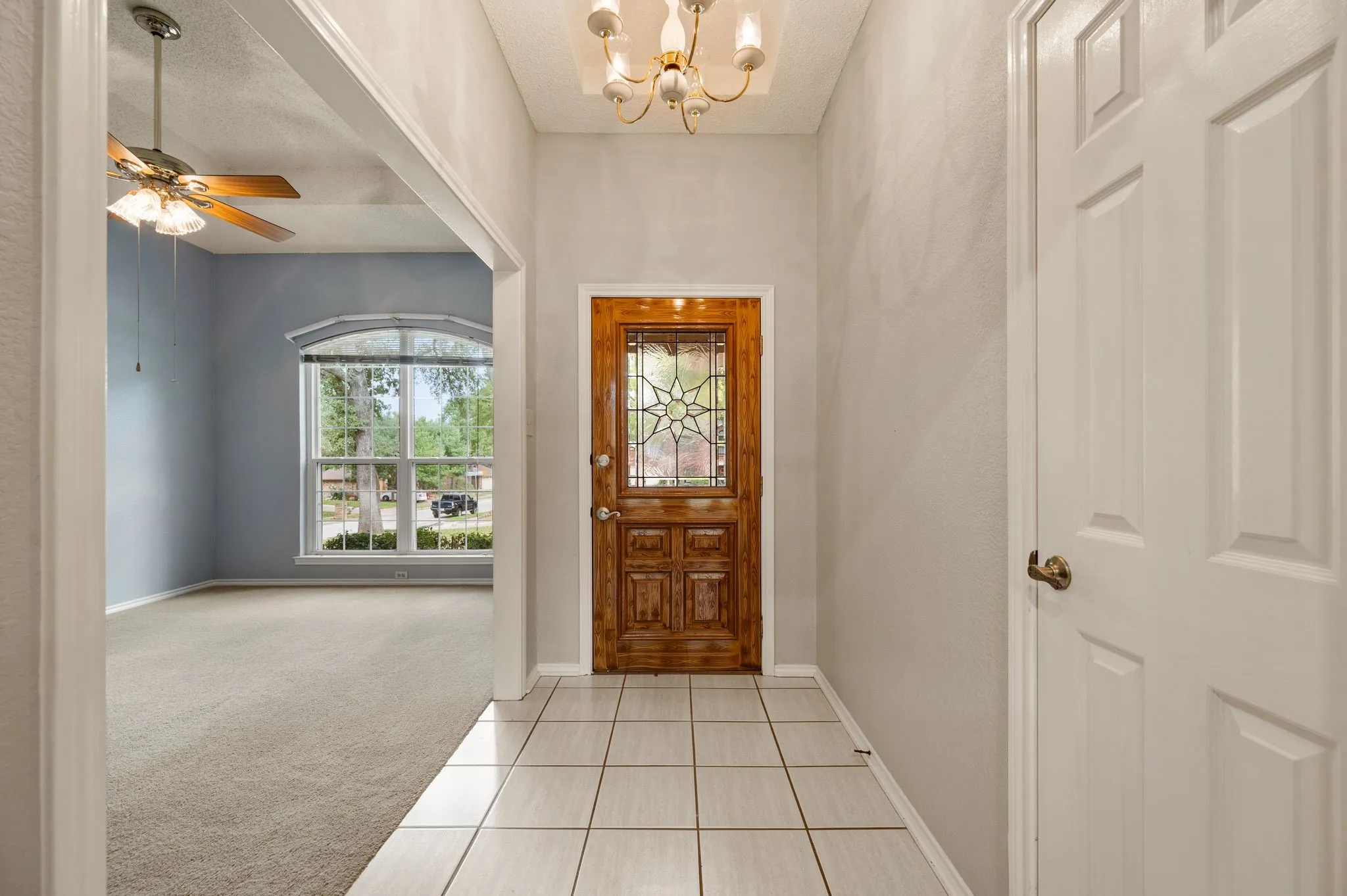 Entryway featuring a wood-finish entry door with a decorative glass insert, ceramic tile flooring, a multi-arm chandelier, and a ceiling fan with integrated lighting