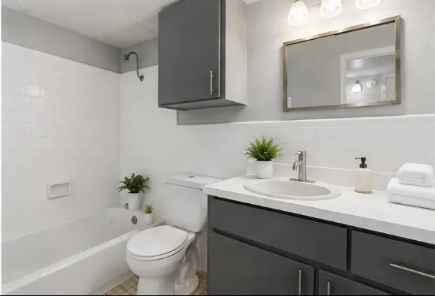 White subway tile shower surround, built-in vanity with dark cabinetry, white countertop, and an oval undermount sink, complemented by a rectangular framed mirror and wall-mounted light fixture