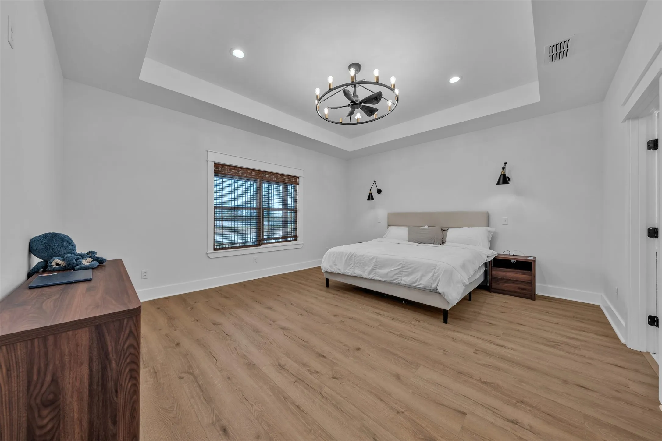 Tray ceiling with a modern chandelier, wood-finish flooring, and wall-mounted sconces