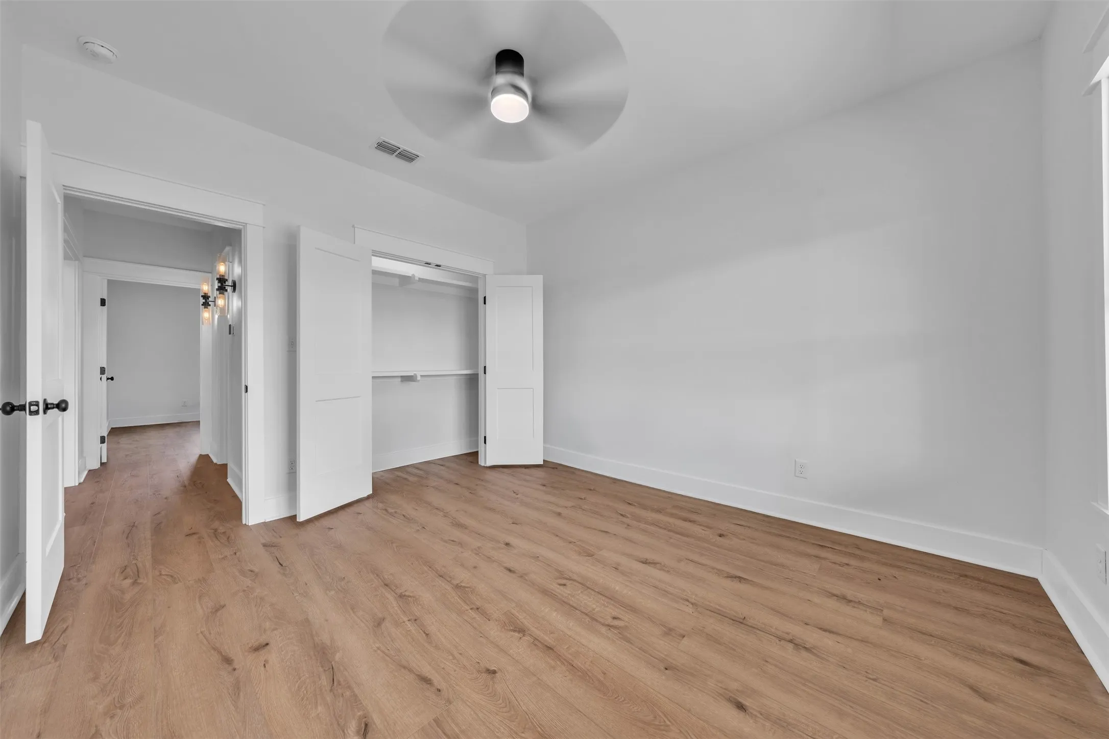 Wood-finish flooring, white walls, ceiling fan, bi-fold closet doors, and black door hardware