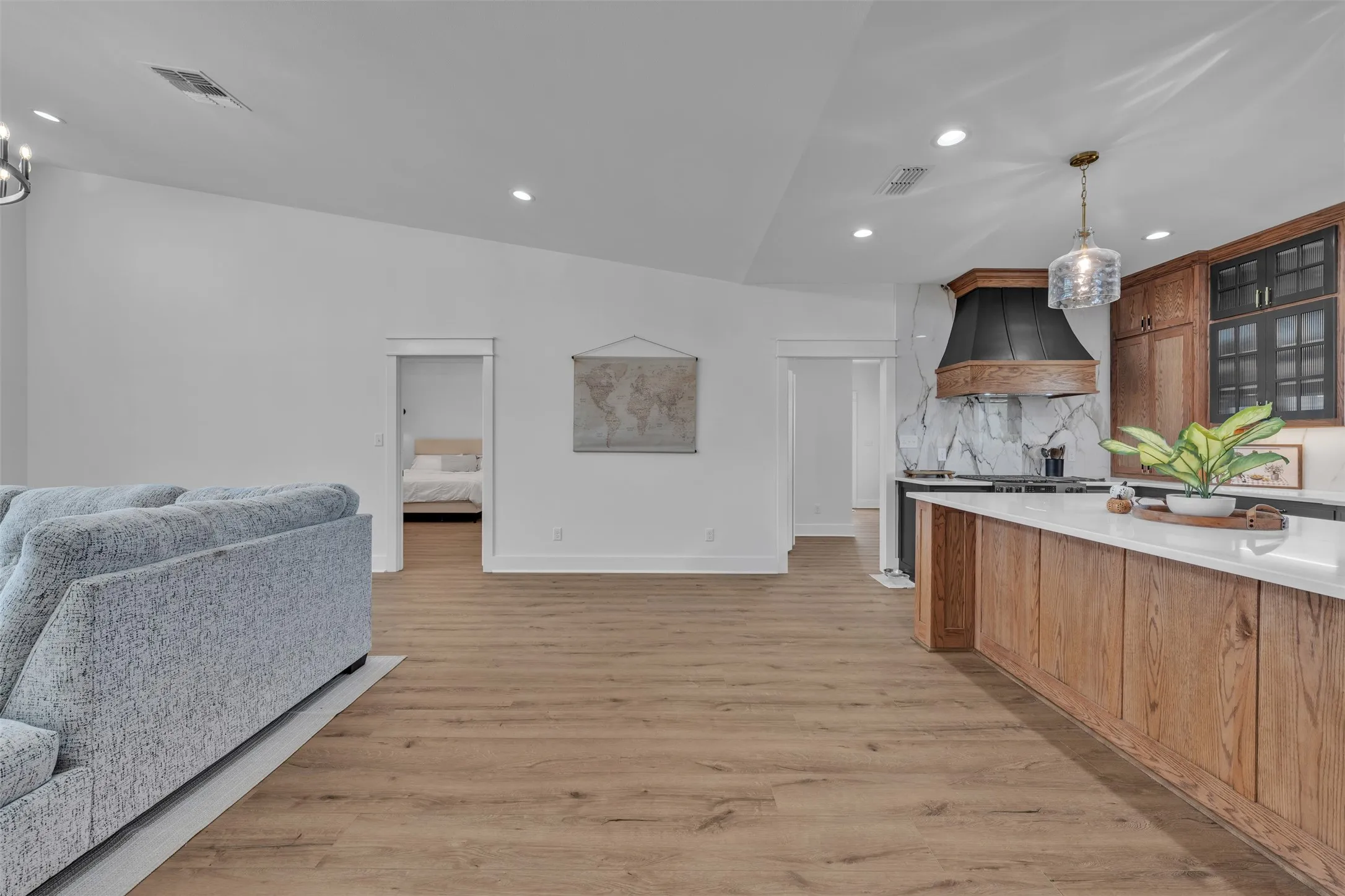 Wood-finish flooring throughout, vaulted ceilings, recessed lighting, kitchen island with a white countertop, and a decorative range hood